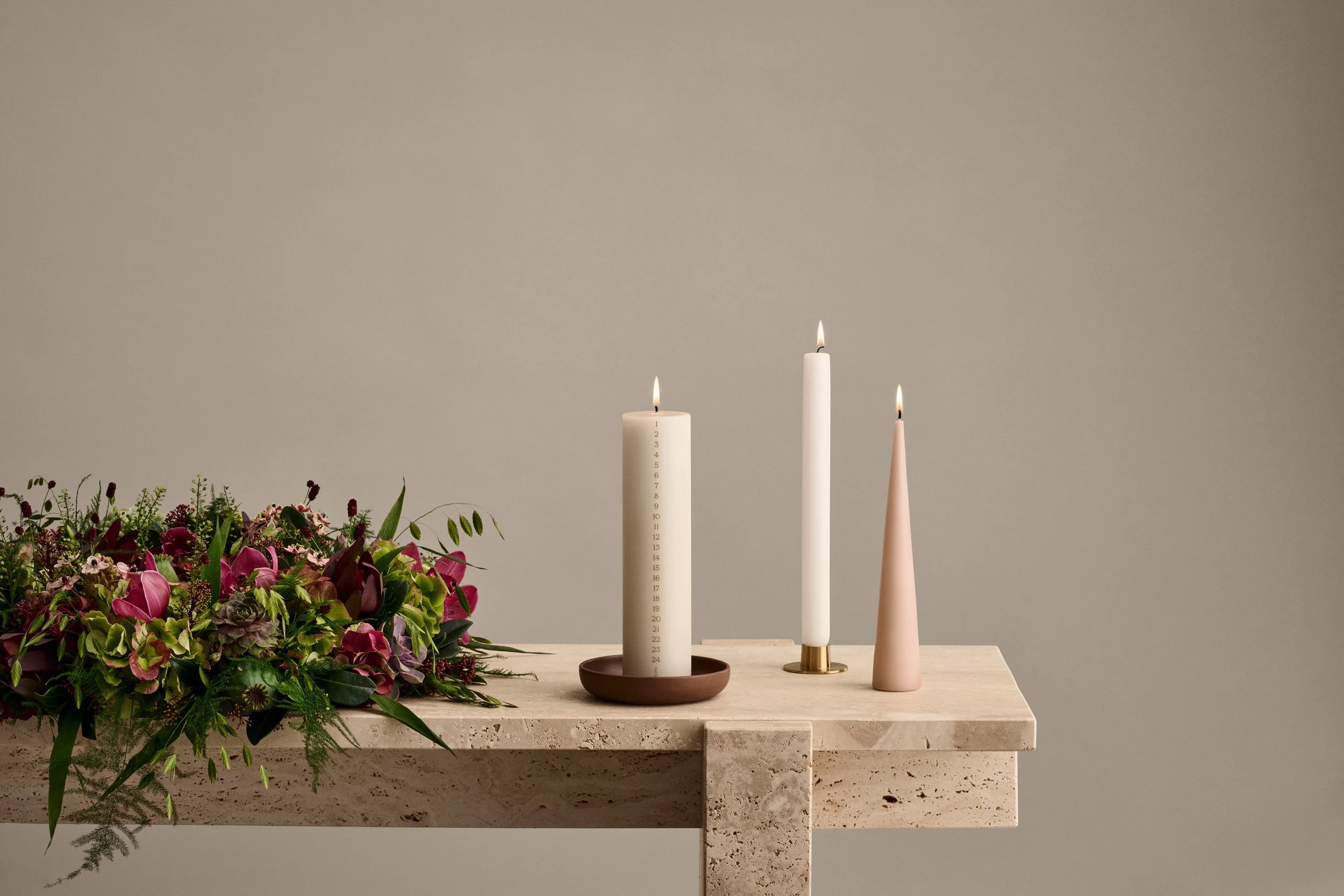 Scandinavian Christmas display featuring an Ester & Erik white Advent calendar candle, taper candles, and a lush holiday wreath on a travertine table.