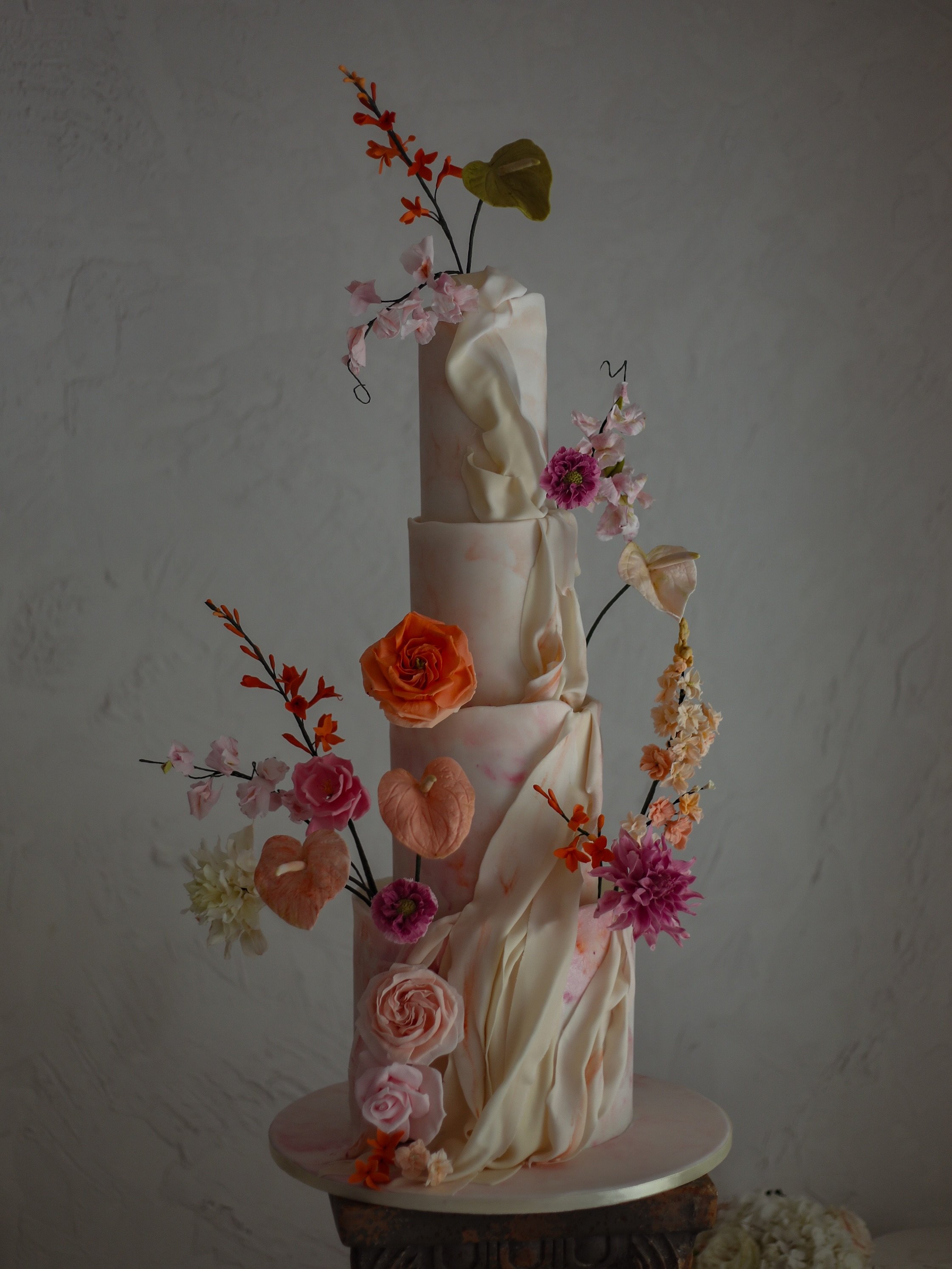 Autumn romance, sculpted in sugar. A celebration of movement, texture and colour, this towering wedding cake brings together delicate sugar flowers in rich autumnal hues with dramatic fondant draping that cascades effortlessly across each tier. What 