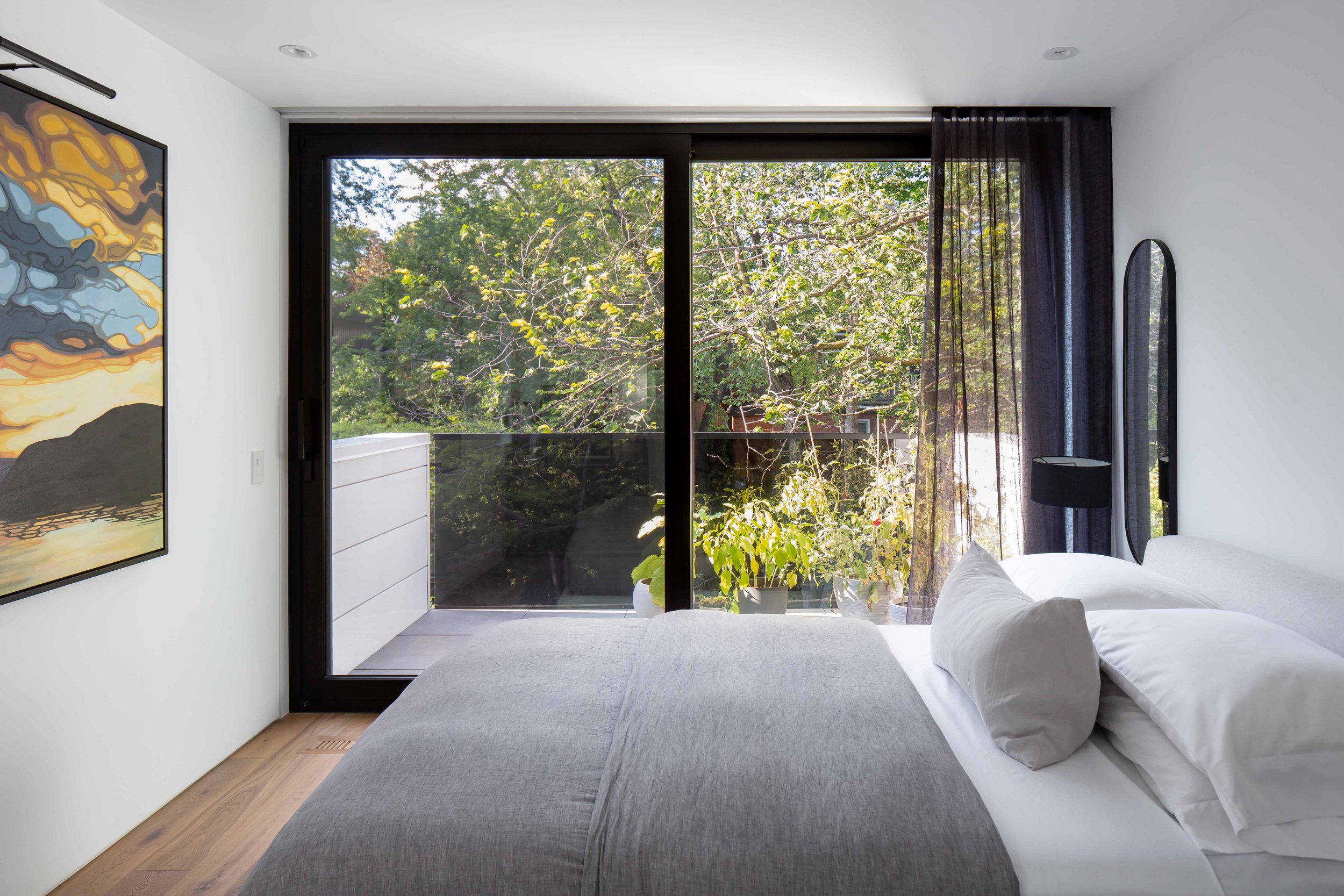Modern primary bedroom suite with walkout balcony framing Toronto tree canopy