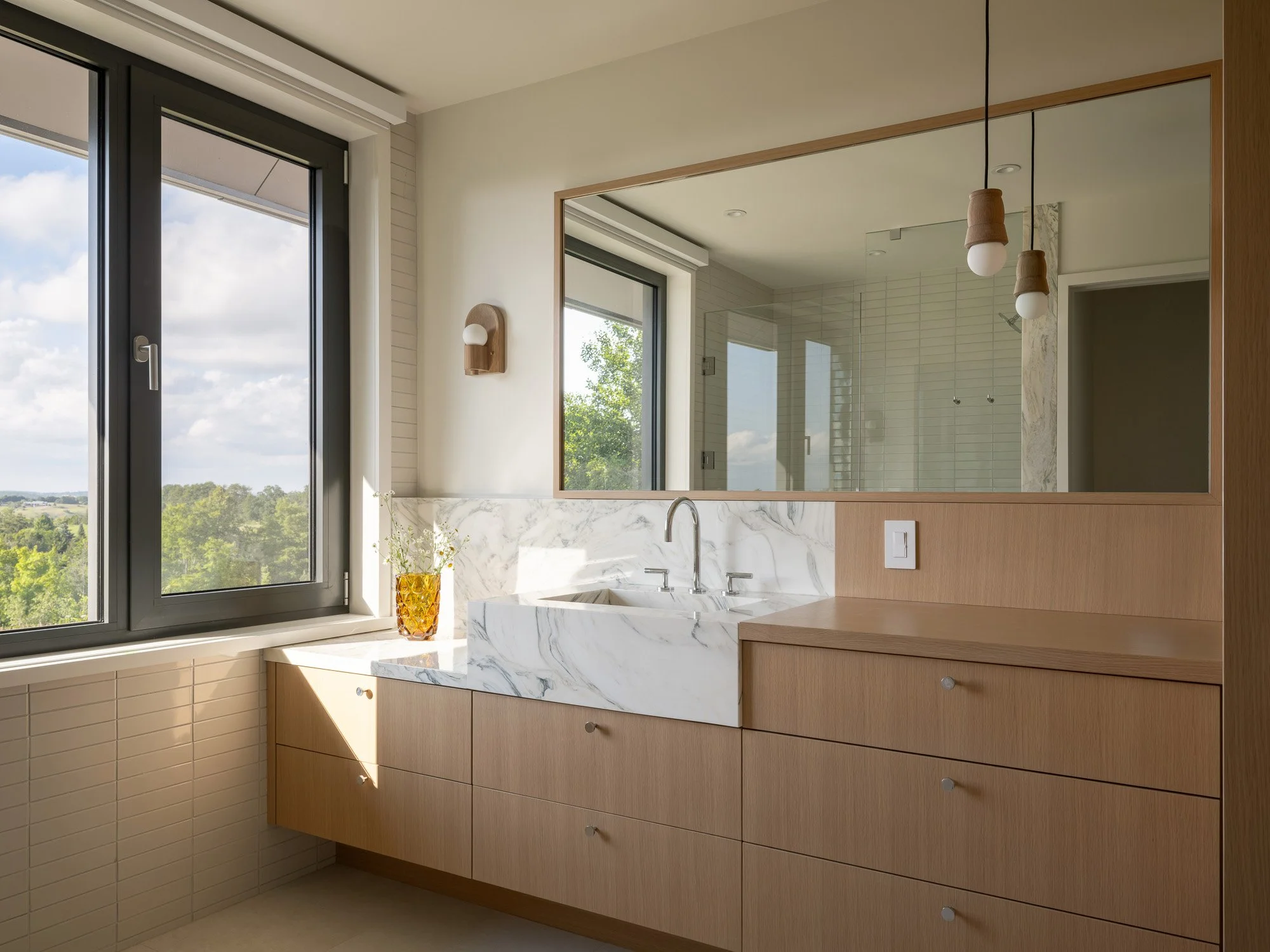 Close-up of bespoke bathroom millwork seamlessly integrated with stone countertops, vanity mirrors, and natural window lighting.