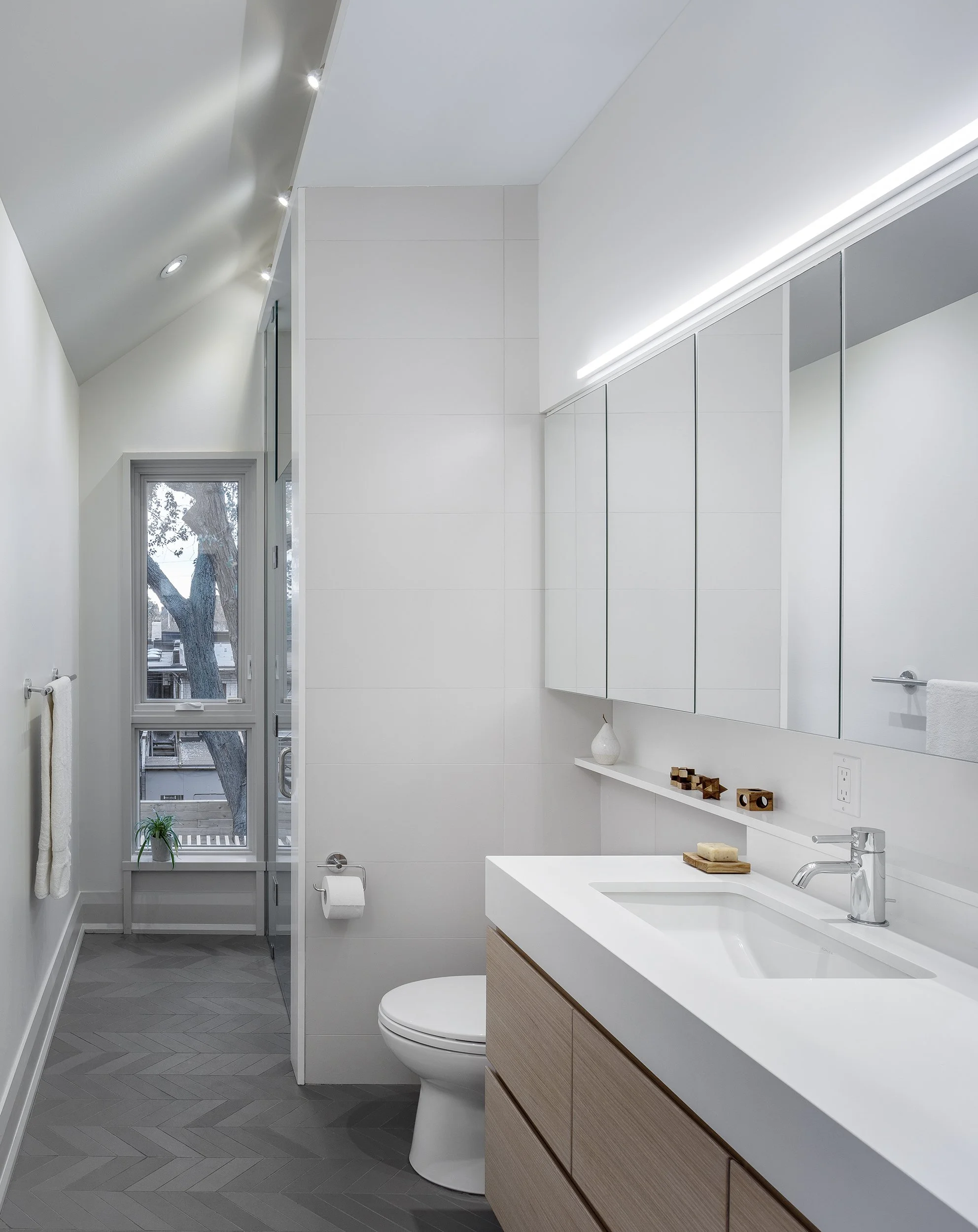 Modern primary bathroom architecture with light grey herringbone tile flooring and bespoke wood millwork vanity