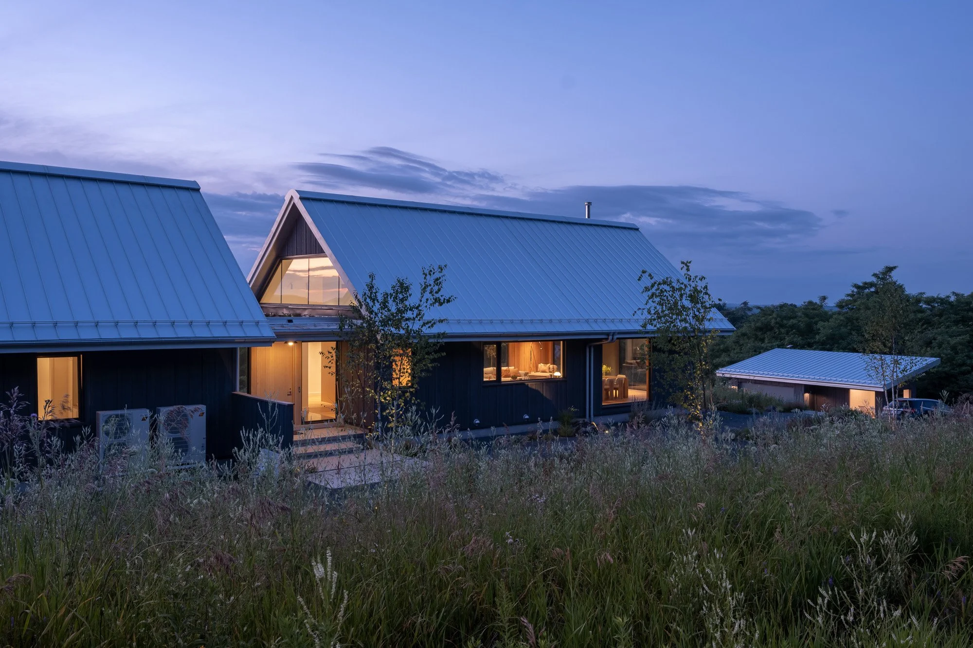 Modern country home exterior at dusk showcasing a detached garage and warm architectural lighting reflecting vernacular design influences.