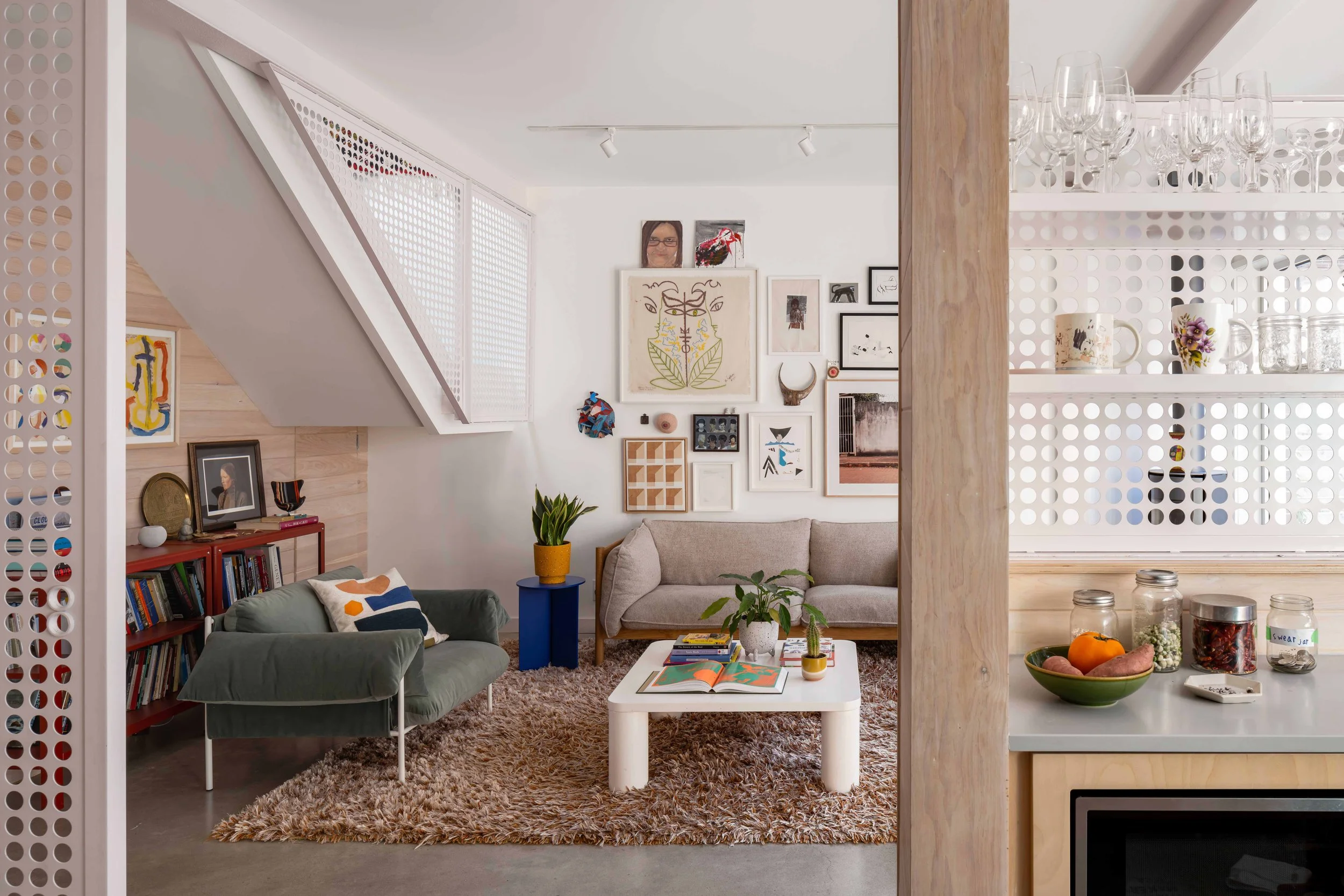 A bright, compact residential living space inside a warehouse conversion showcasing a distinct pink-painted structural steel beam