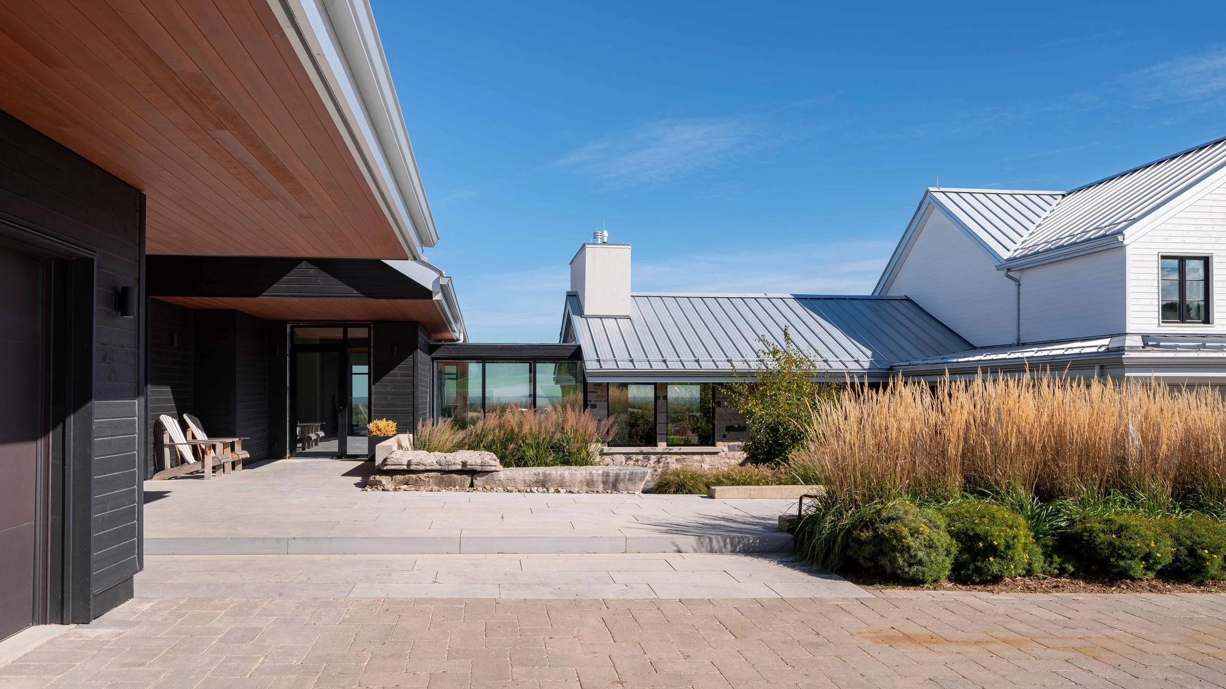 Architectural entrance view highlighting a modern glass bridge connecting two distinct residential wings over a rolling hillside.