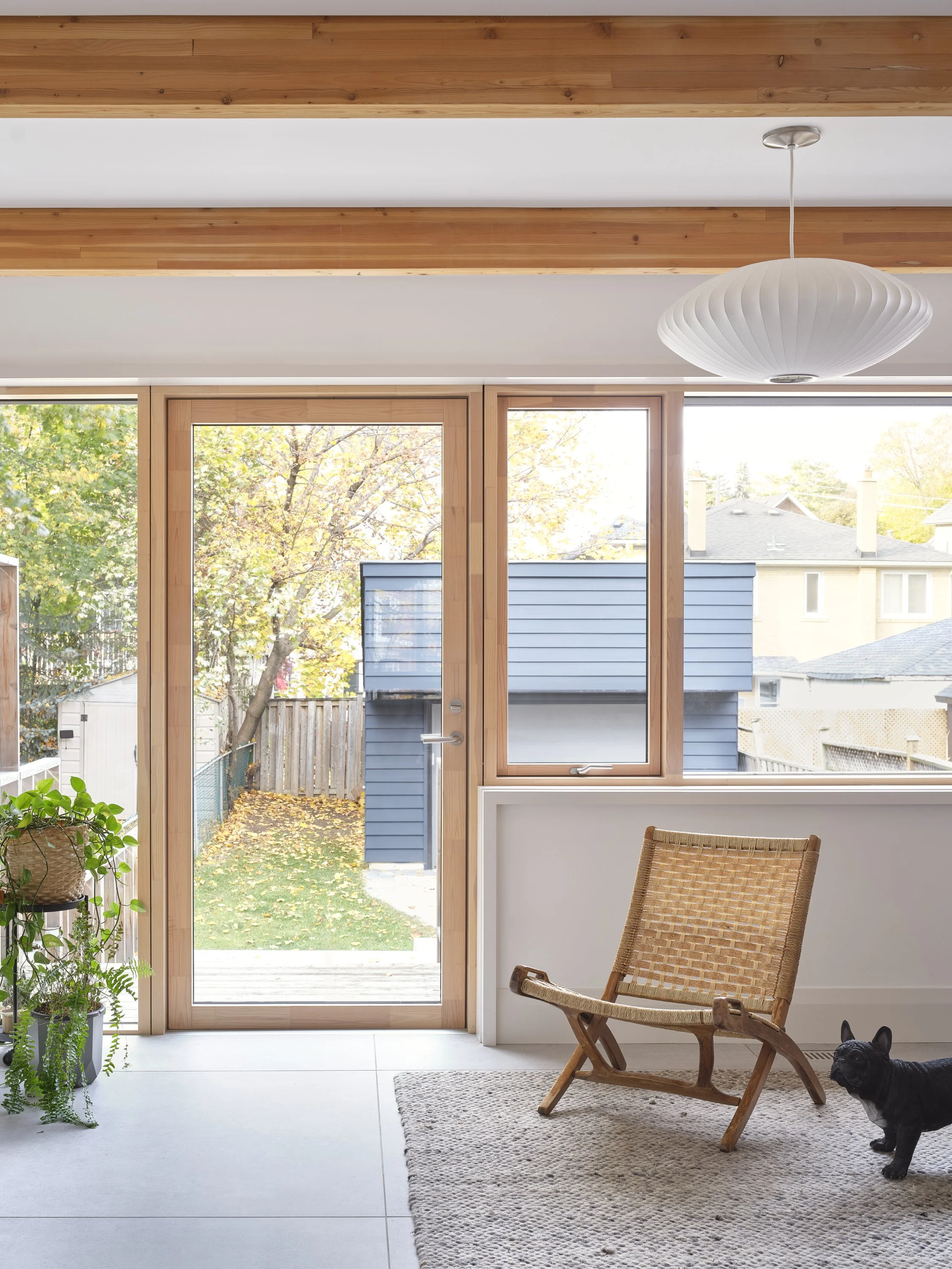 Bright minimalist living room design with exposed glulam ceiling beams looking out to a backyard garden.