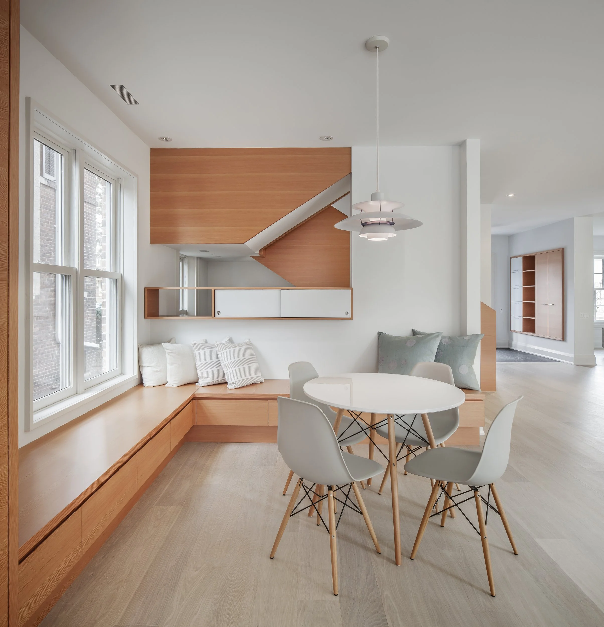 Open concept dining room interior featuring custom Douglas fir millwork banquette seating and a minimalist modern staircase by Wayback Architects