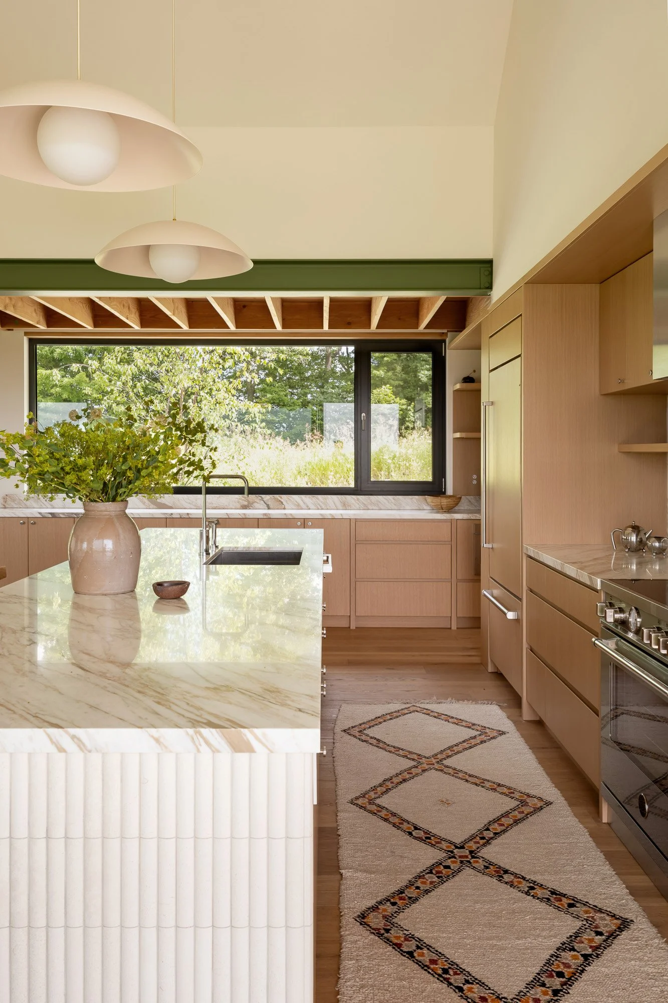 Modern kitchen interior with warm wood cabinetry and exposed green structural steel beams acting as a design accent.