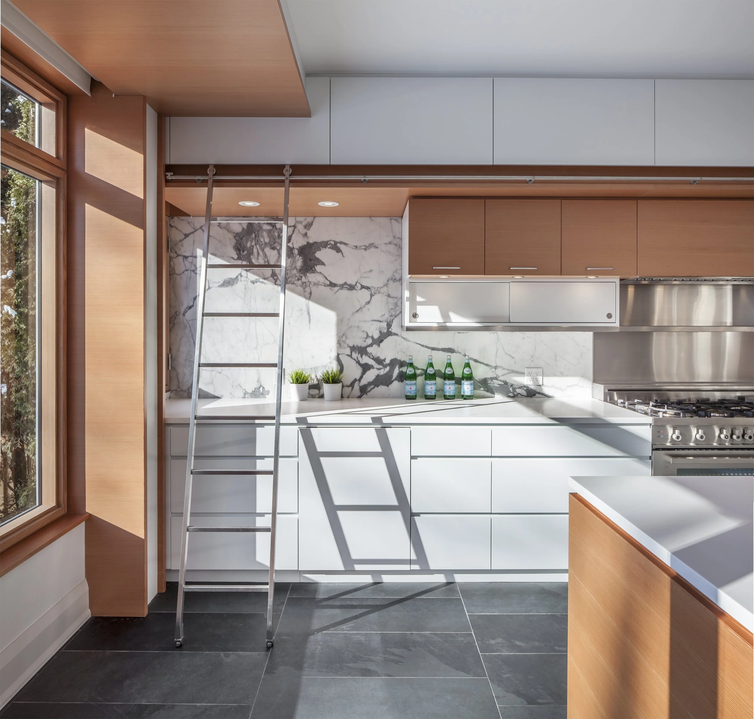 Contemporary minimalist kitchen design with custom built-in Douglas fir cabinets, painted millwork accents, and integrated library ladder.