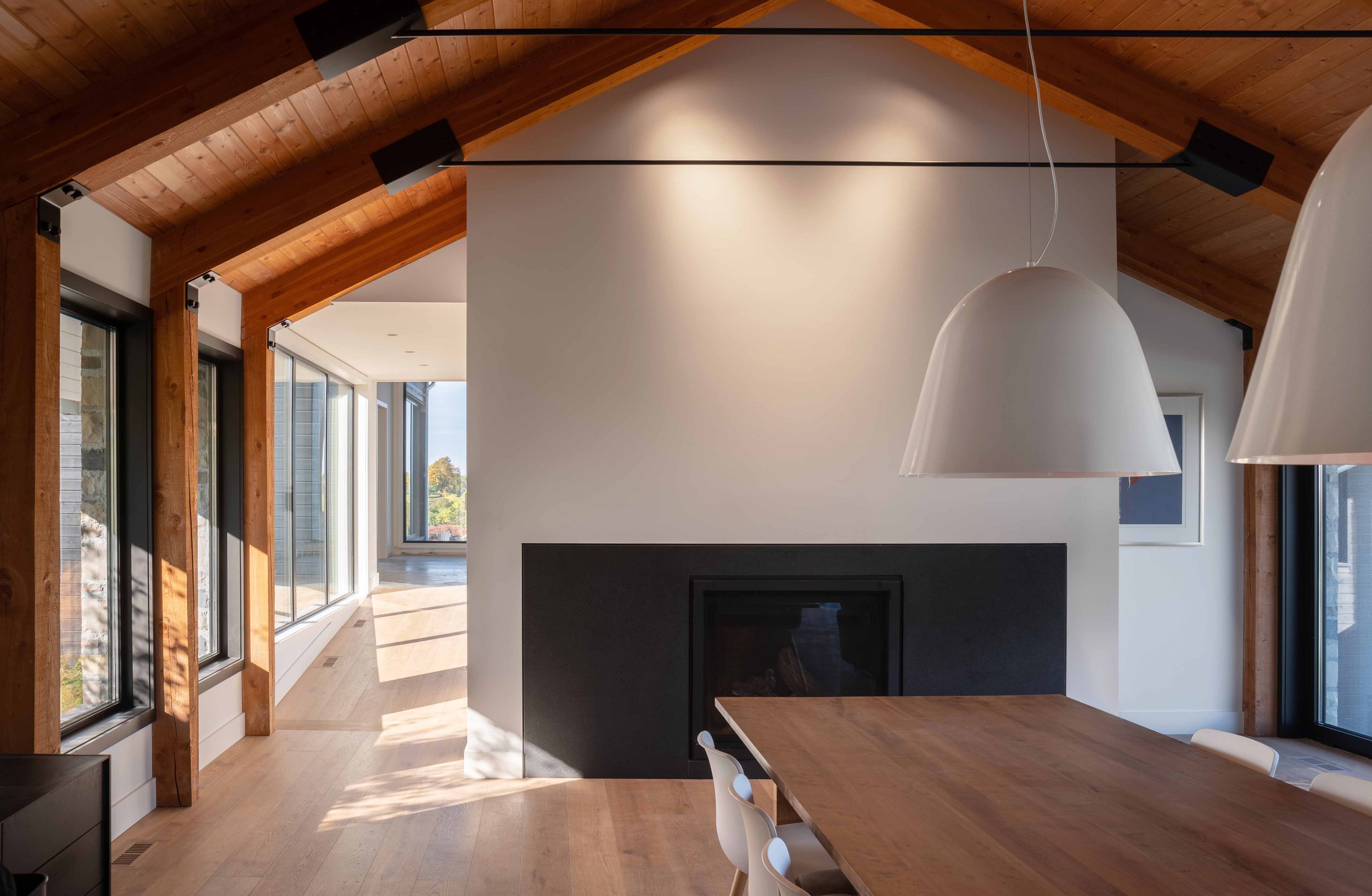 Warm minimalist dining hall interior designed by Wayback Architects featuring a grand stone fireplace for family gatherings.