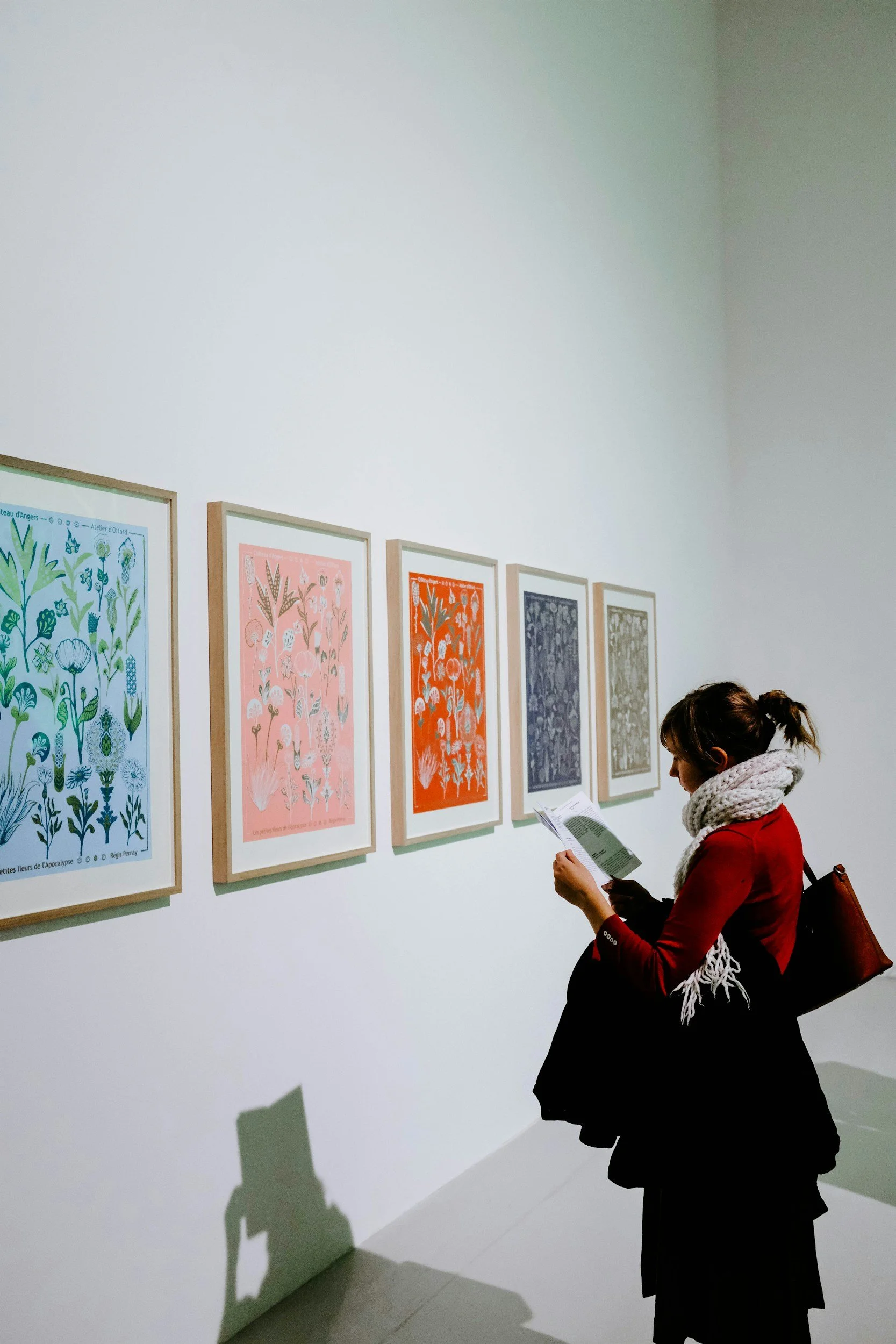 Color photograph of a woman standing in front of colorful artworks, installed in a gallery.