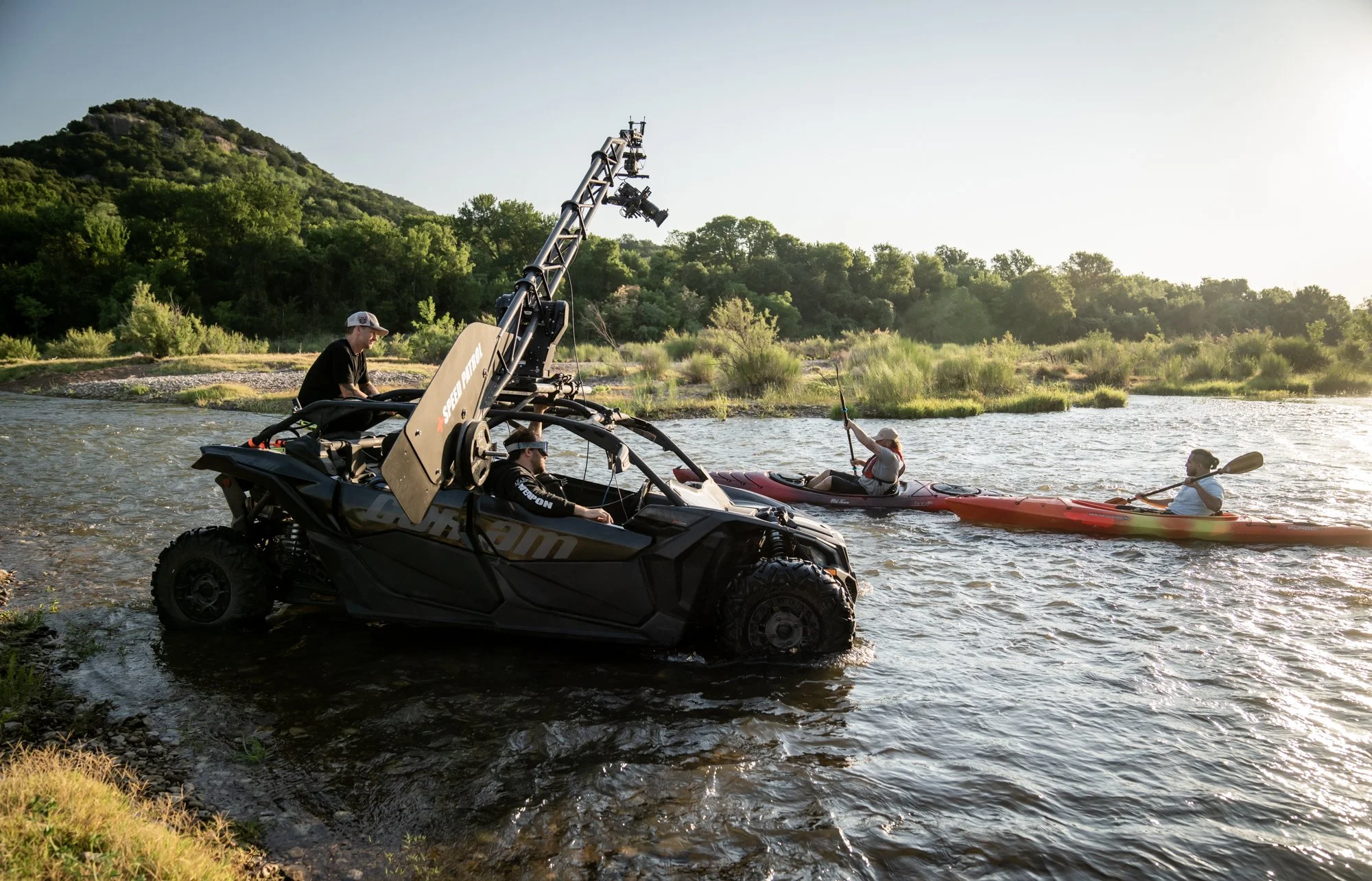 A utility vehicle enters a creek beside a kayaker during lifestyle commercial production.