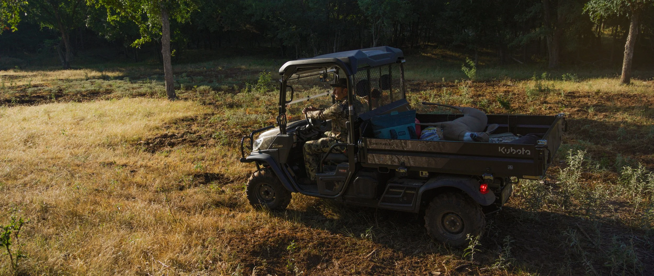 A utility vehicle loaded with gear waits in a sunlit field for an outdoor commercial scene.