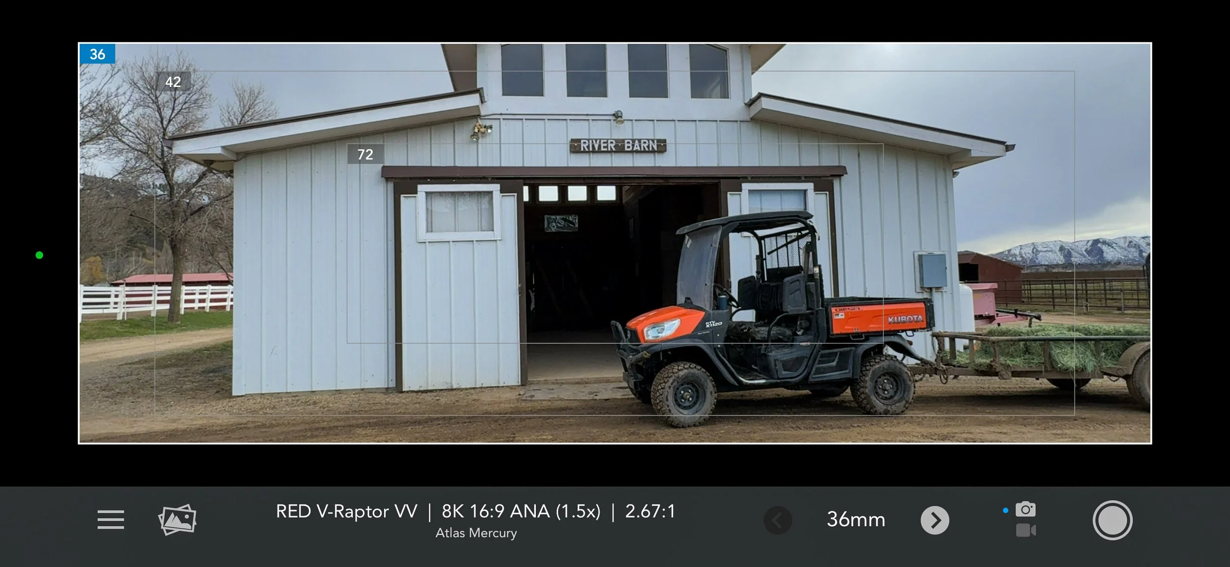 An orange utility vehicle sits in a barn doorway within a production monitor frame.