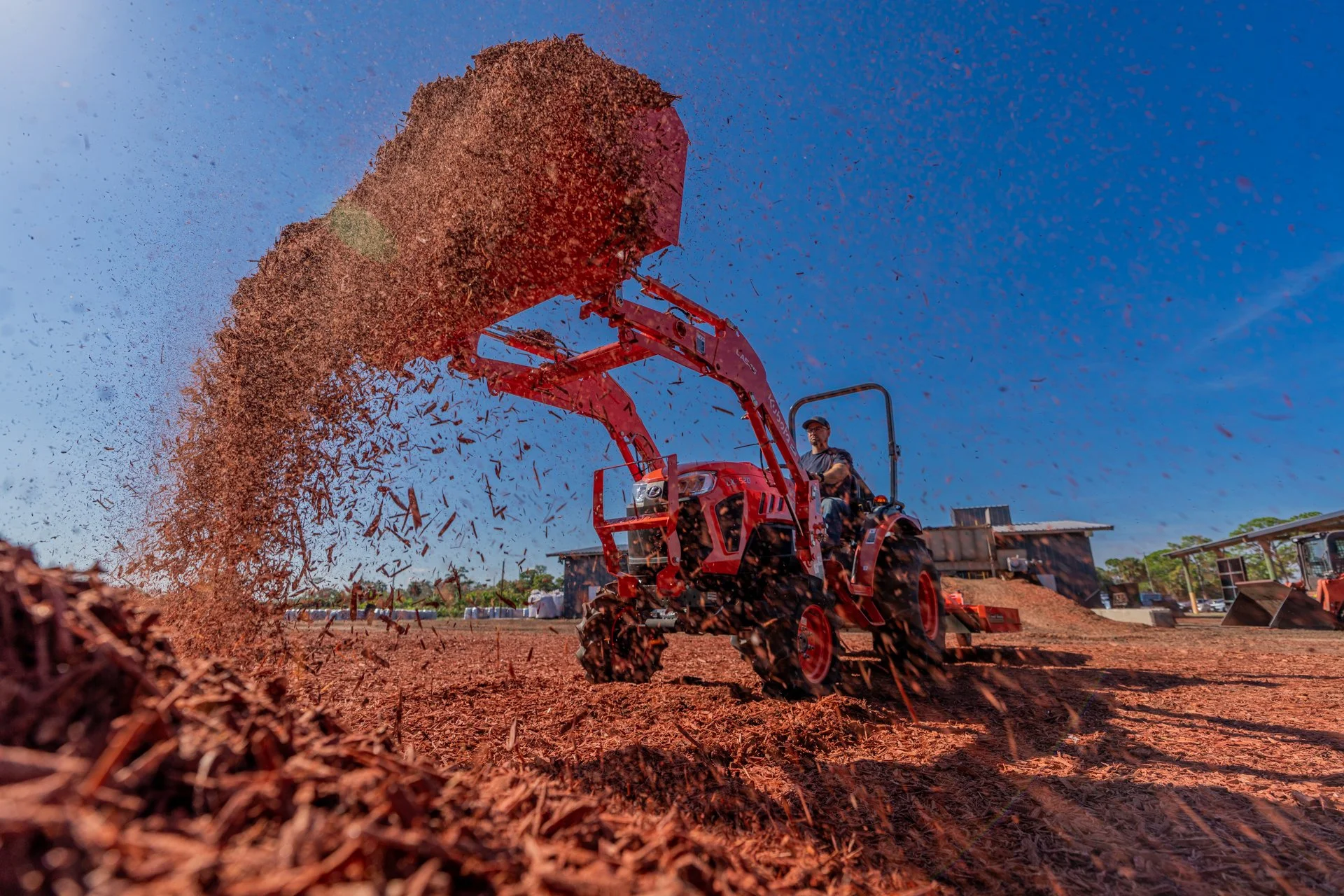 An orange machine throws a high arc of soil across a freshly worked field in an agriculture commercial.