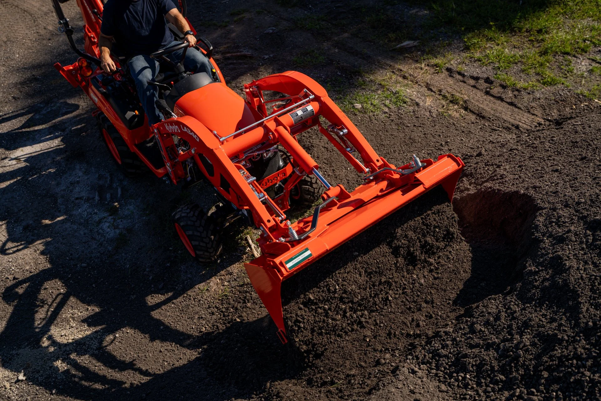 An overhead view shows an orange tractor attachment digging into dark soil.