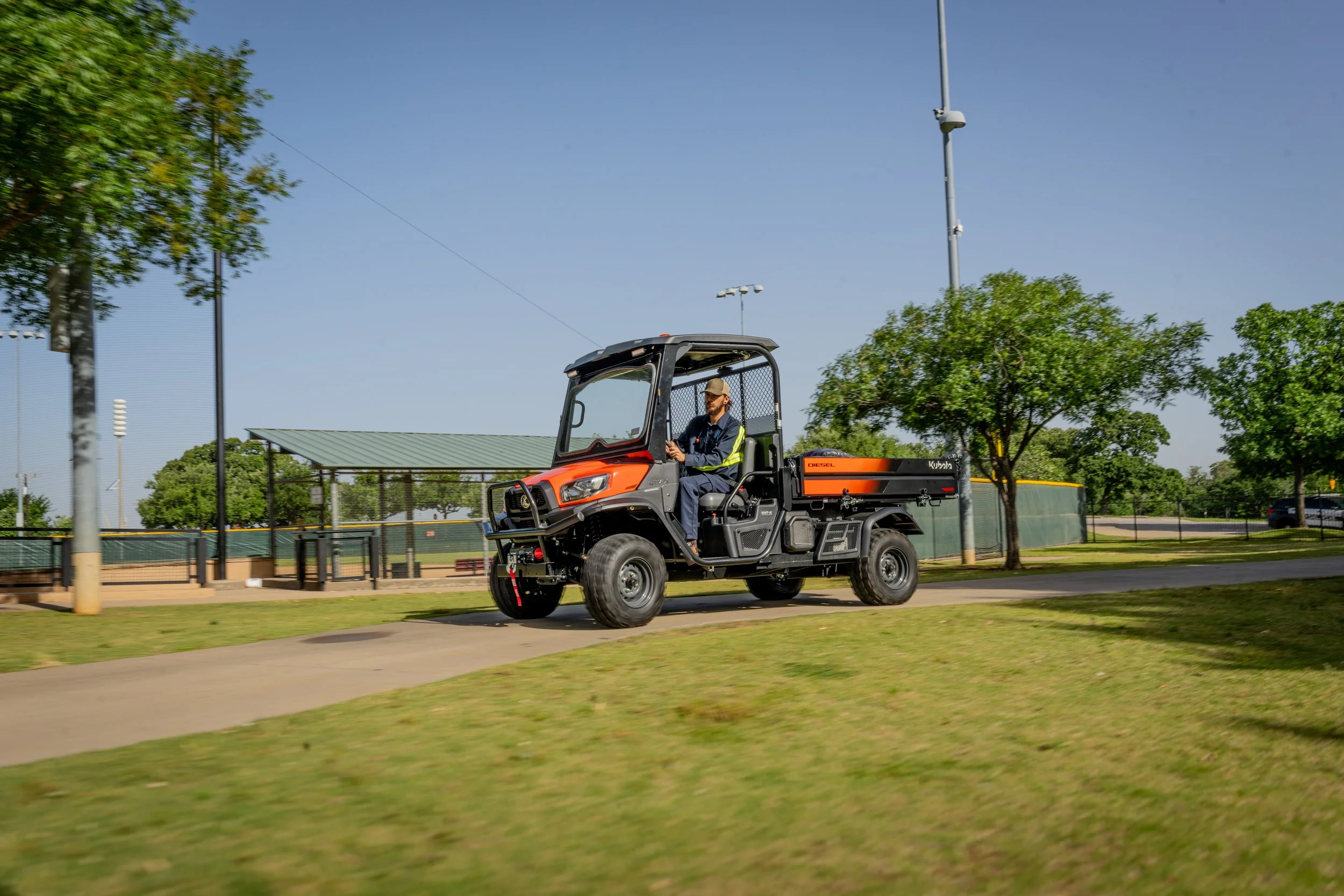 An orange utility vehicle travels along a paved path through a landscaped park.