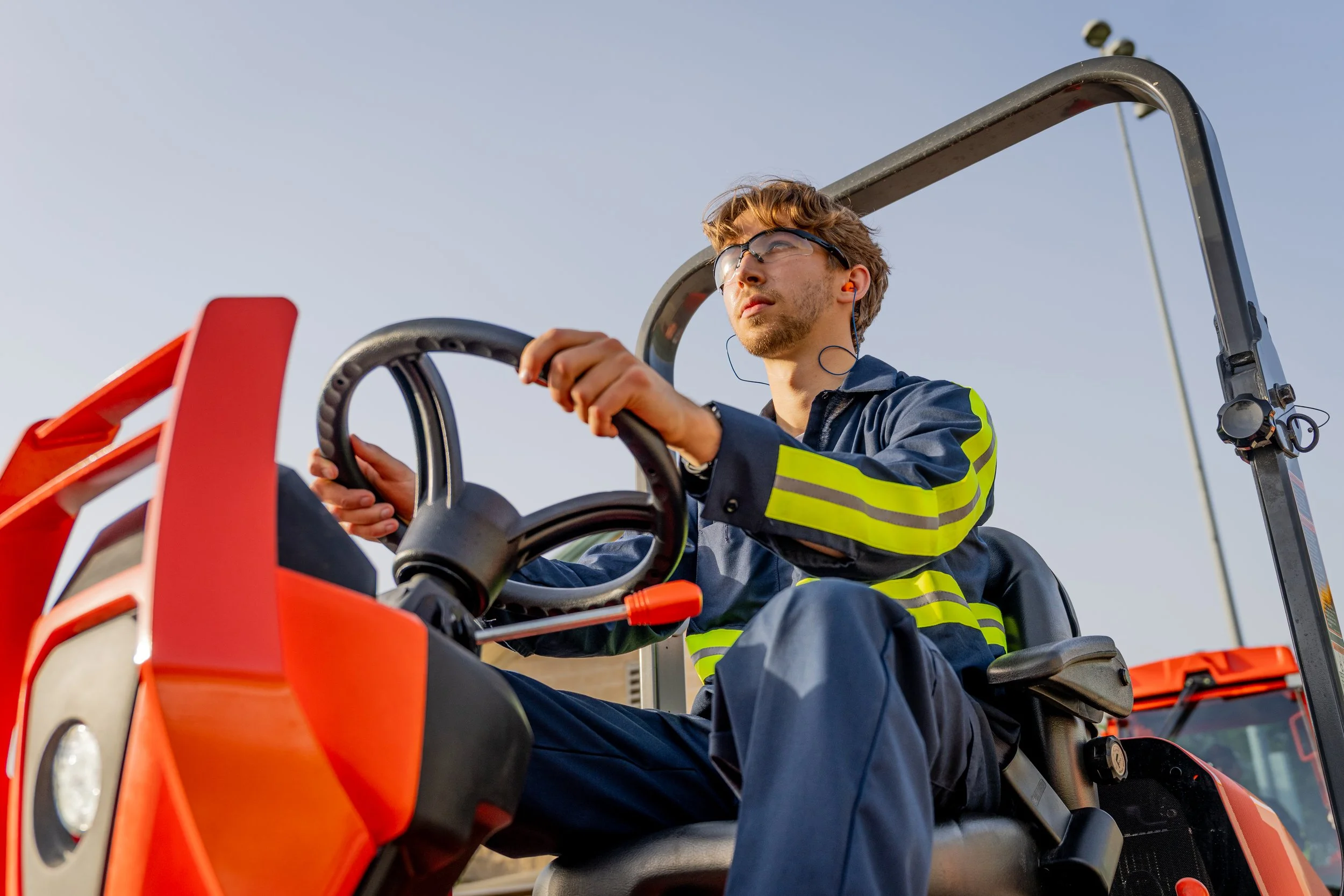 An operator drives an orange tractor in a bright product video production scene.