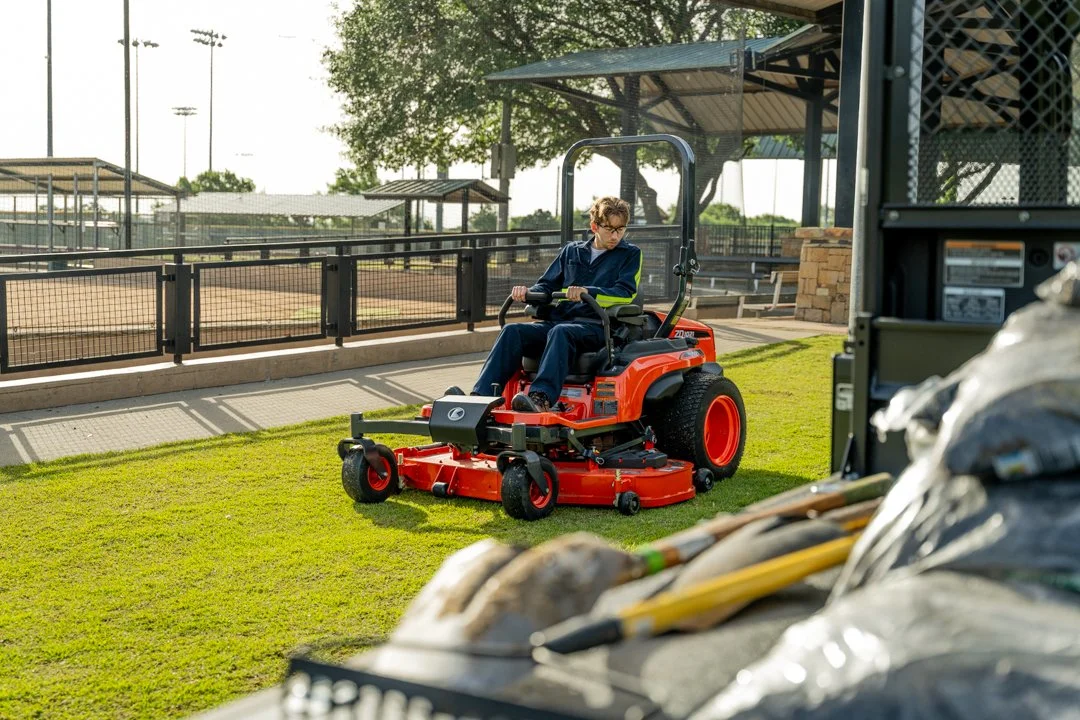 An operator steers an orange mower across a neatly cut lawn beside a fence.