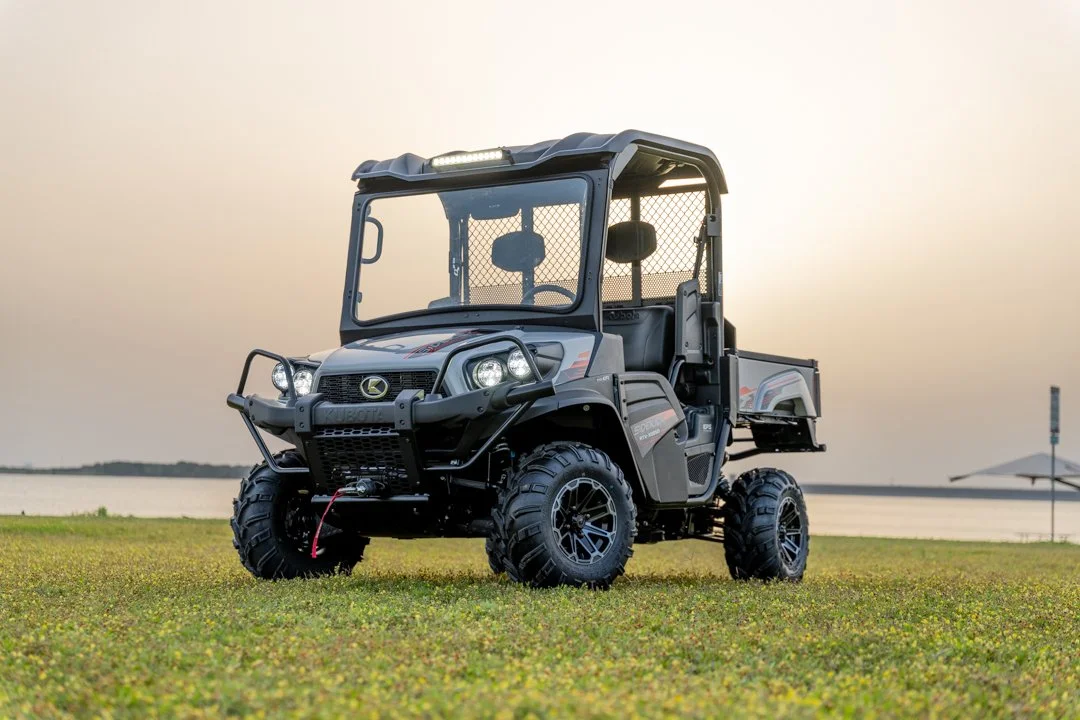 A black utility vehicle is presented on grass beside a calm lake under a clear sky.