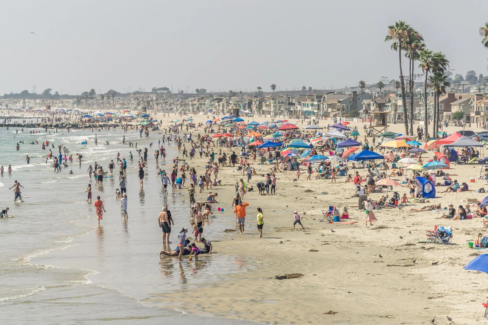 view from Newport Beach pier on a Sunny day overlooking the crowded beach of swimmers