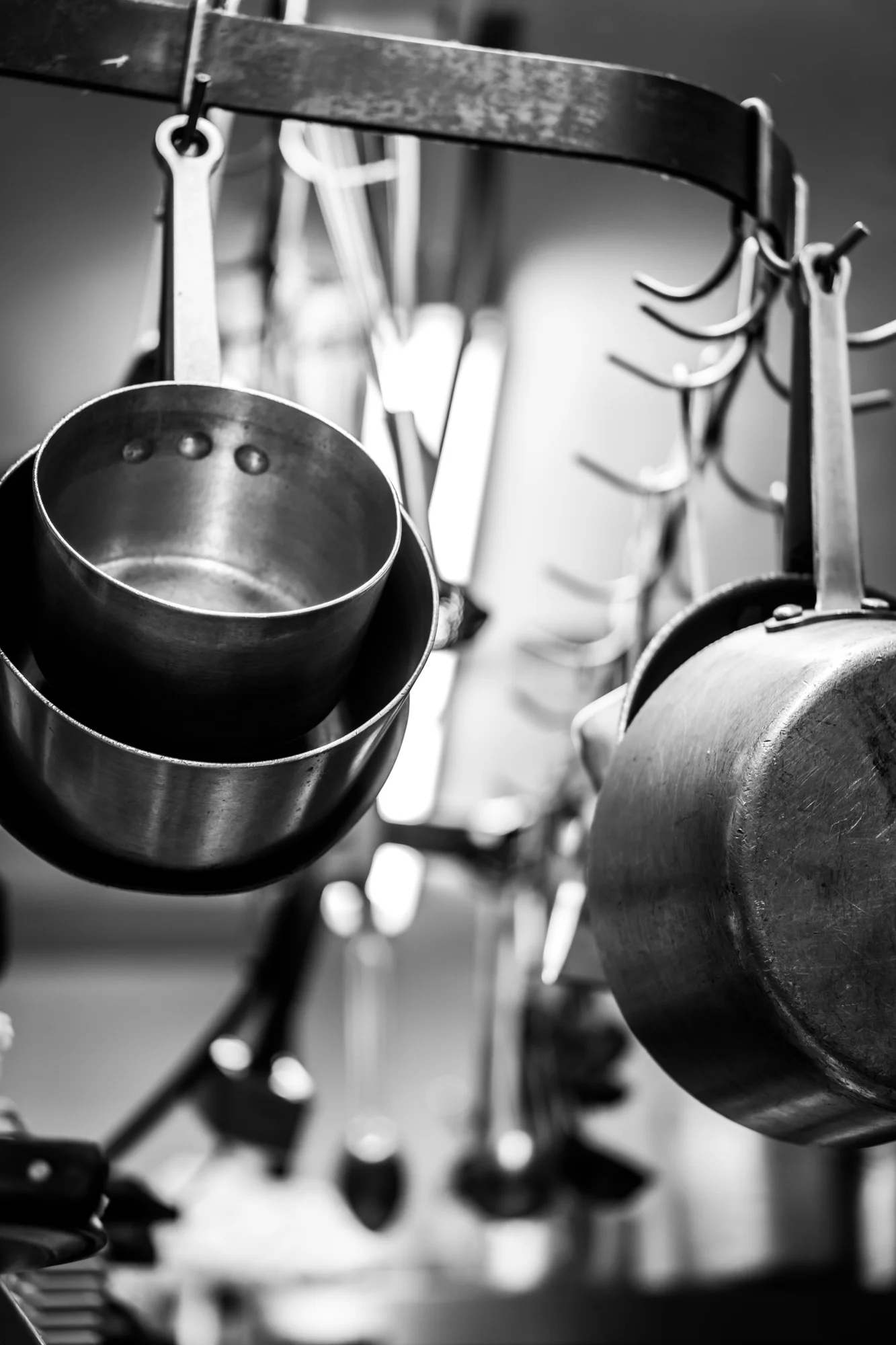 Restaurant photography By Joseph Barber Studios of Black and white photo of kitchen pots and pans hanging at the Royal hen restaurant In Balboa Island