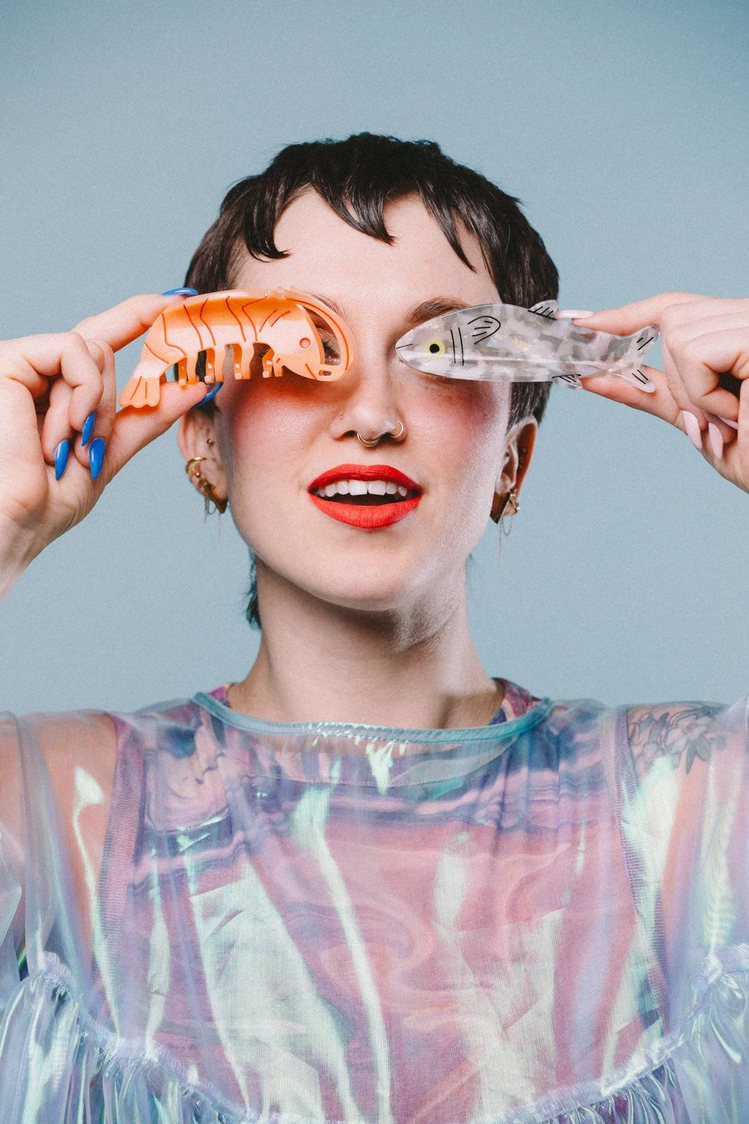 A girl with short spiky bangs and a shimmery shirt holding plastic shrimp and fish in front of her eyes.