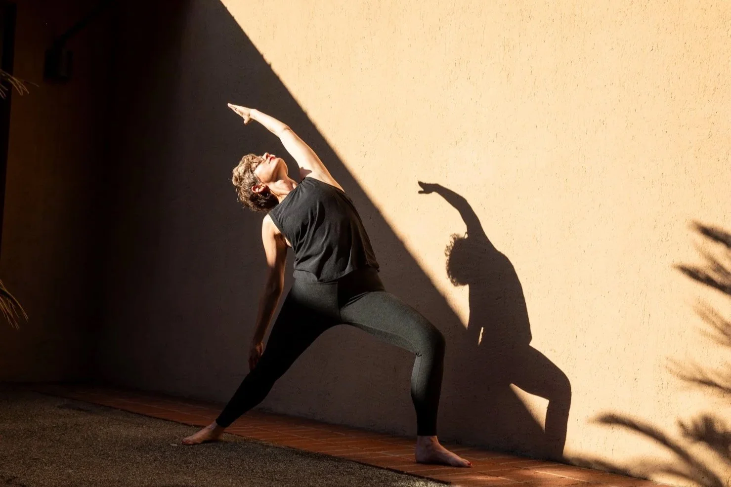 A woman doing a yoga pose against a wall with a geometric shadow.