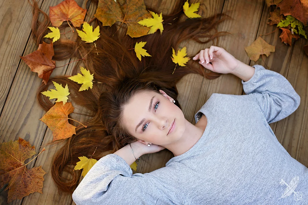 Huntington North senior Kaitlyn lays in yellow leaves for her senior pictures with feather and key.