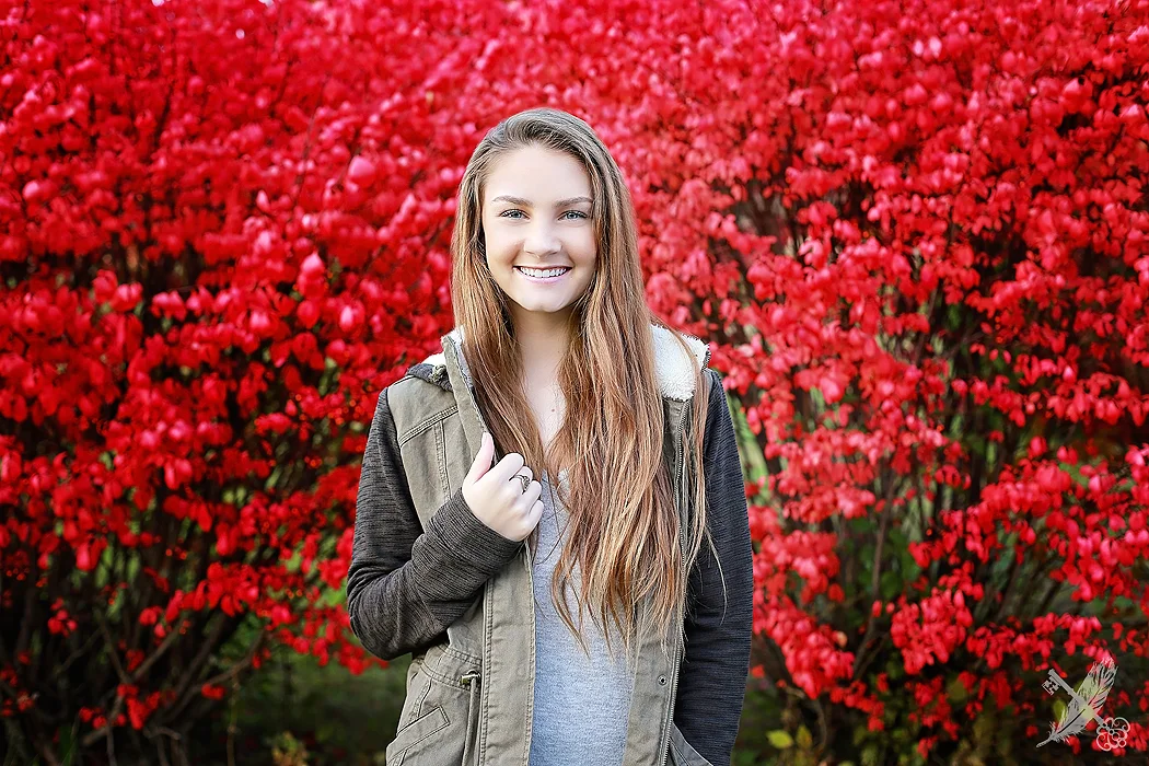 Huntington Senior in front of vibrant red trees for senior pictures with feather and key photographer.