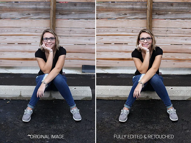 A high school senior girl sits, smiling on a parking block in downtown Huntington IN in front of a wood pallet wall.