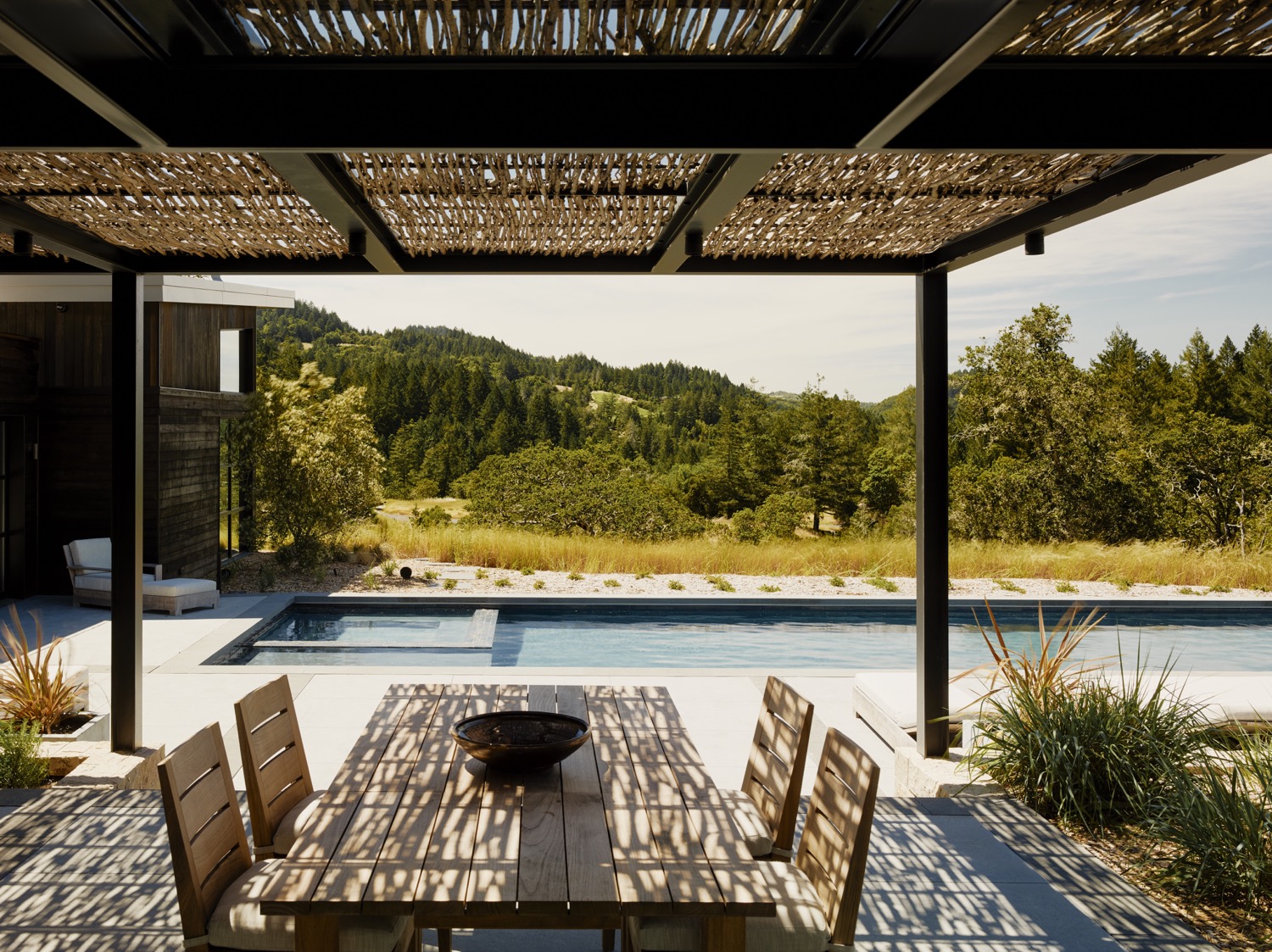 The outdoor dining is shaded by woven willow branches on a metal arbor.