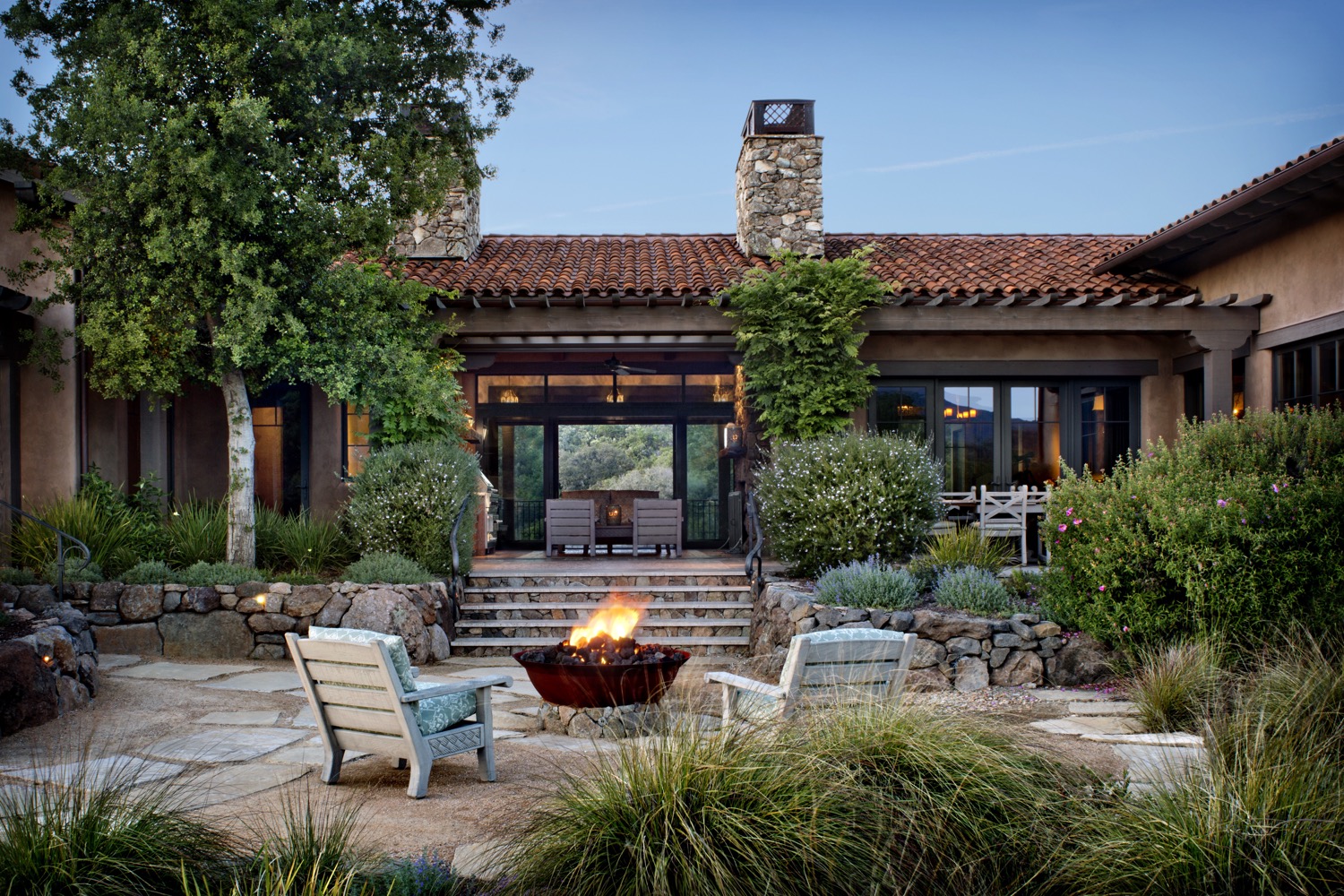 The buff-colored paving stones anchor a rustic seating area around the firepit.