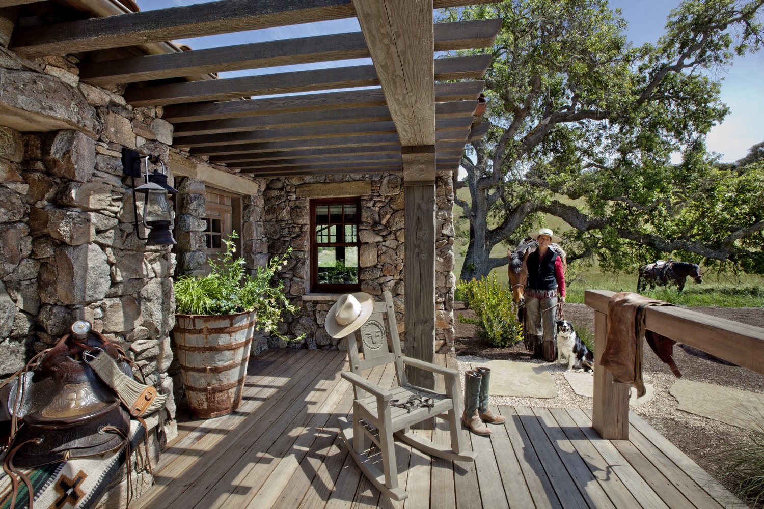 The ranch manager for the Santa Lucia Preserve is smiling with two horses and a dog, near the porch of the guesthouse.