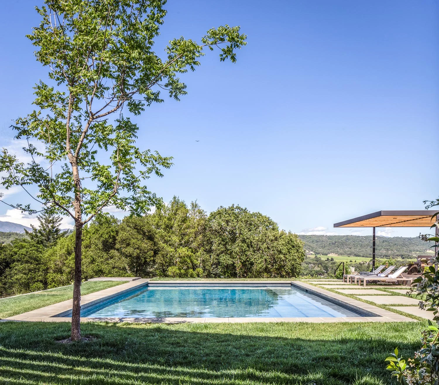 An overview of the pool, with the covered seating area and concrete pavers to the right.