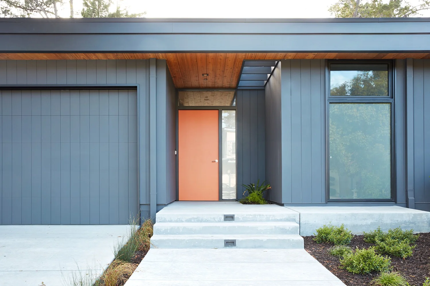 The front door is a pop of orange on a medium gray building.