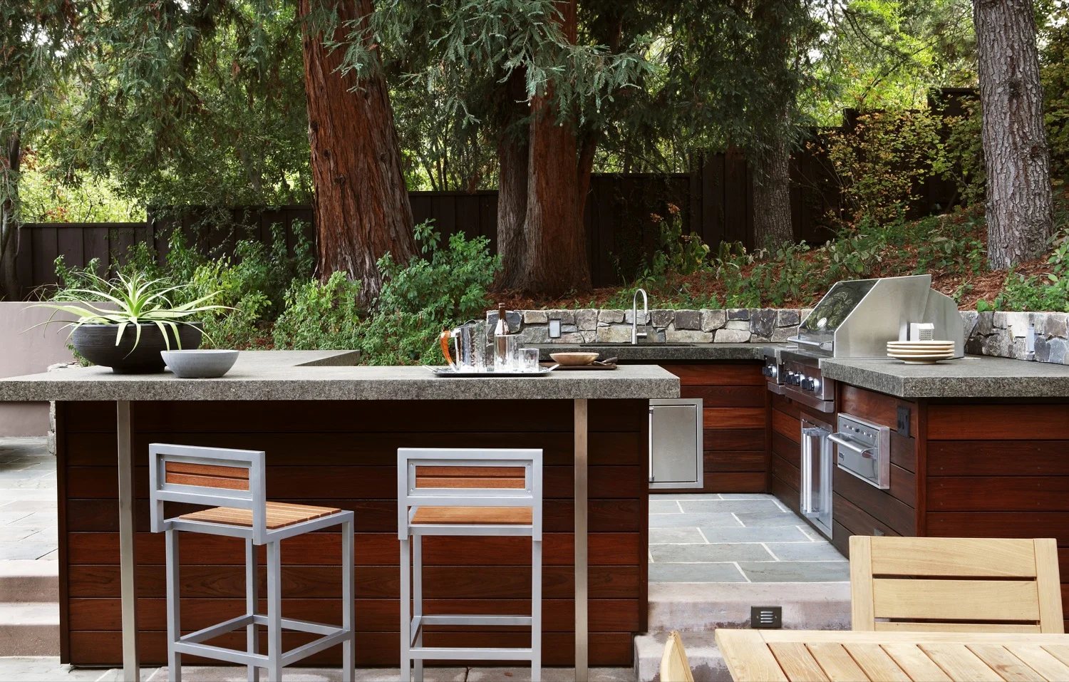The large outdoor kitchen features the rich, dark tones of ipe wood, with a BBQ and a bar counter.