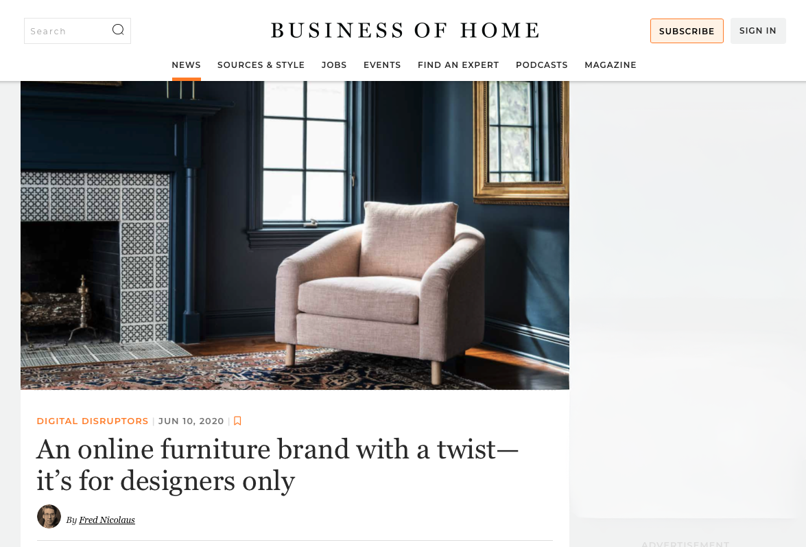 A blush pink linen Saltwolf Hawthorne armchair in a room with dark blue walls, a fireplace with patterned tiles, a window, and a gold-framed mirror from an article in the Business of Home.