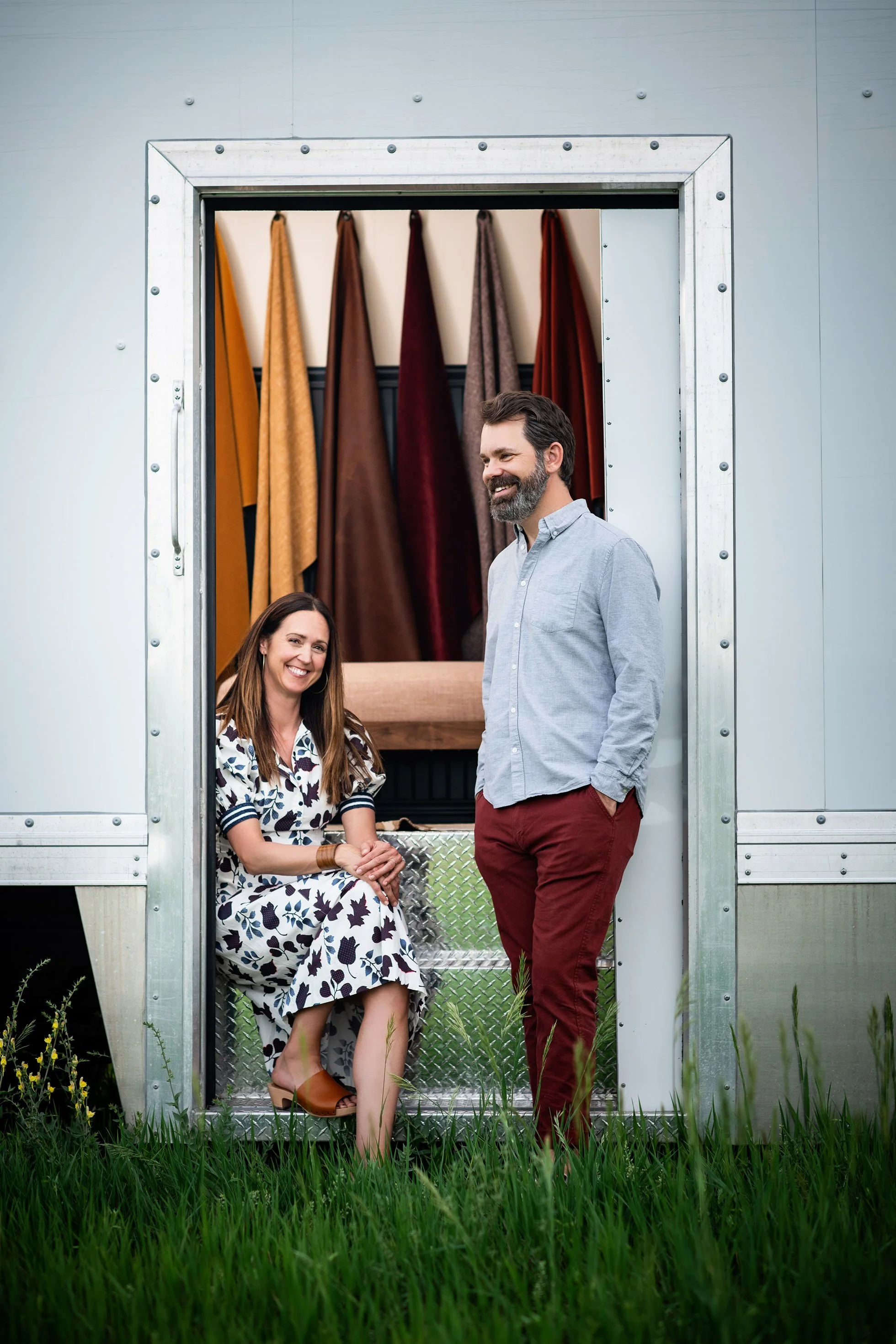 Jordan and Lindy Williams standing in front of the Saltwolf Furniture mobile showroom with fabric swatches hanging behind them.