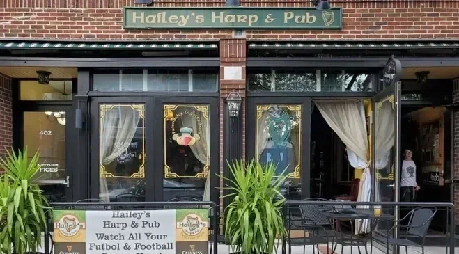 Exterior of Hailey's Harp & Pub with large windows, curtains, plants, and outdoor seating