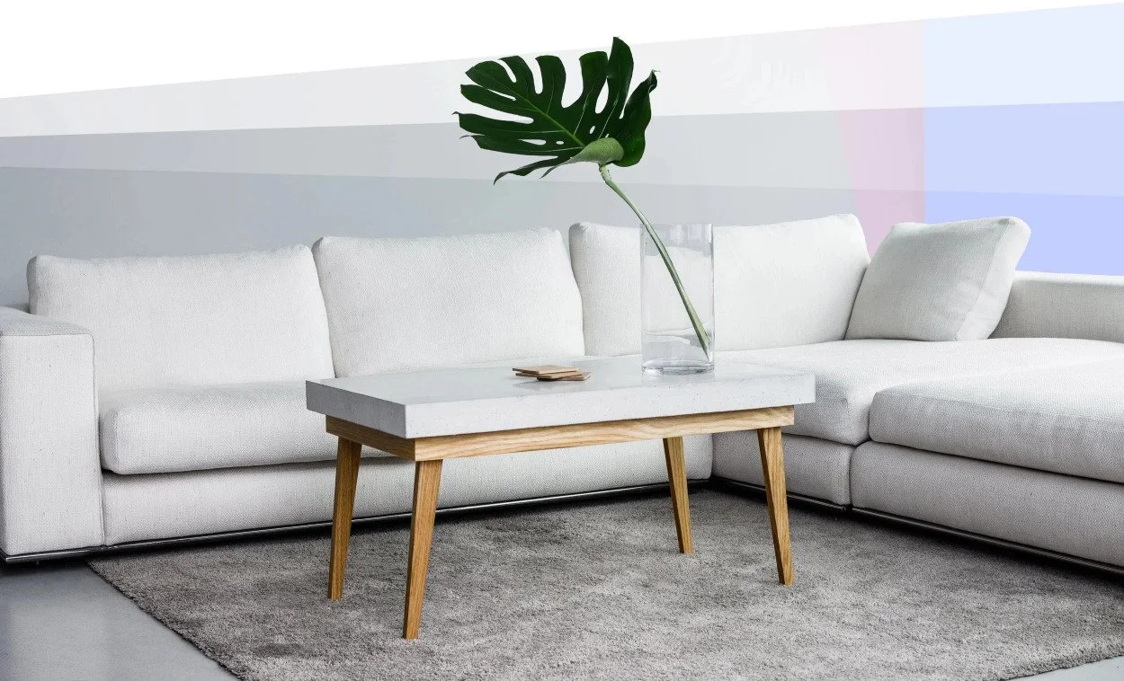 Modern industrial coffee table featuring a polished concrete top and oak-finish tapered legs in a bright living room setting.