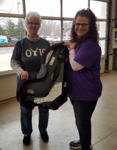 Debra Stall, PER and Suzanne Lewis from the Lodge attaches a sticker stating the car seat was donated from Ravenna Lodge #1076 and assists the Health Educator.