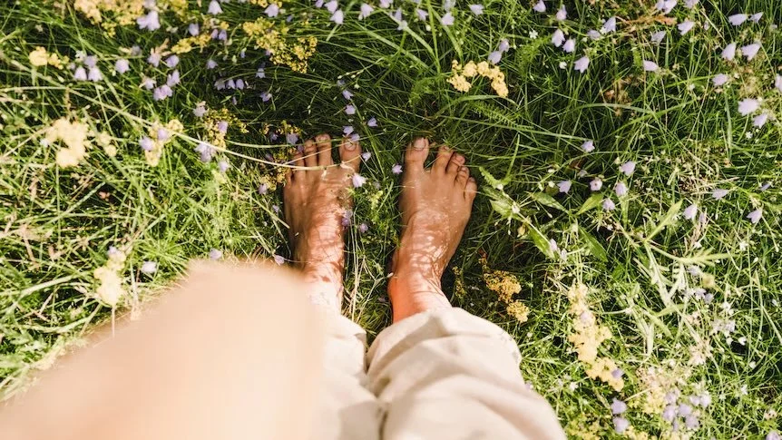 Bare feet standing on green grass with small wildflowers, symbolizing grounding and connection to nature.