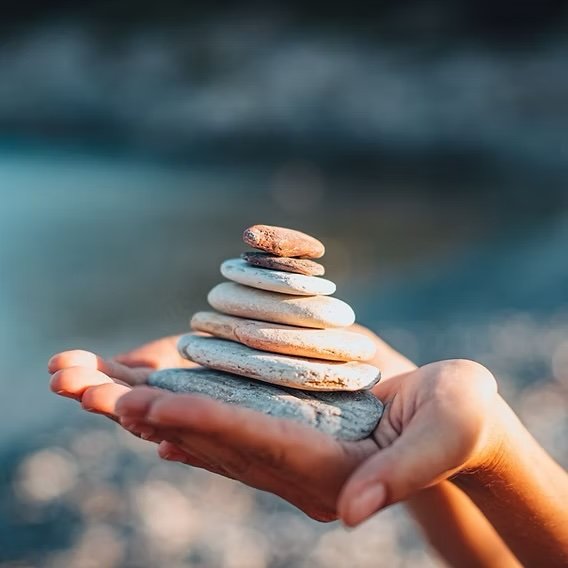 Hands holding a balanced stack of smooth stones, symbolizing mindfulness, calm, and emotional balance.