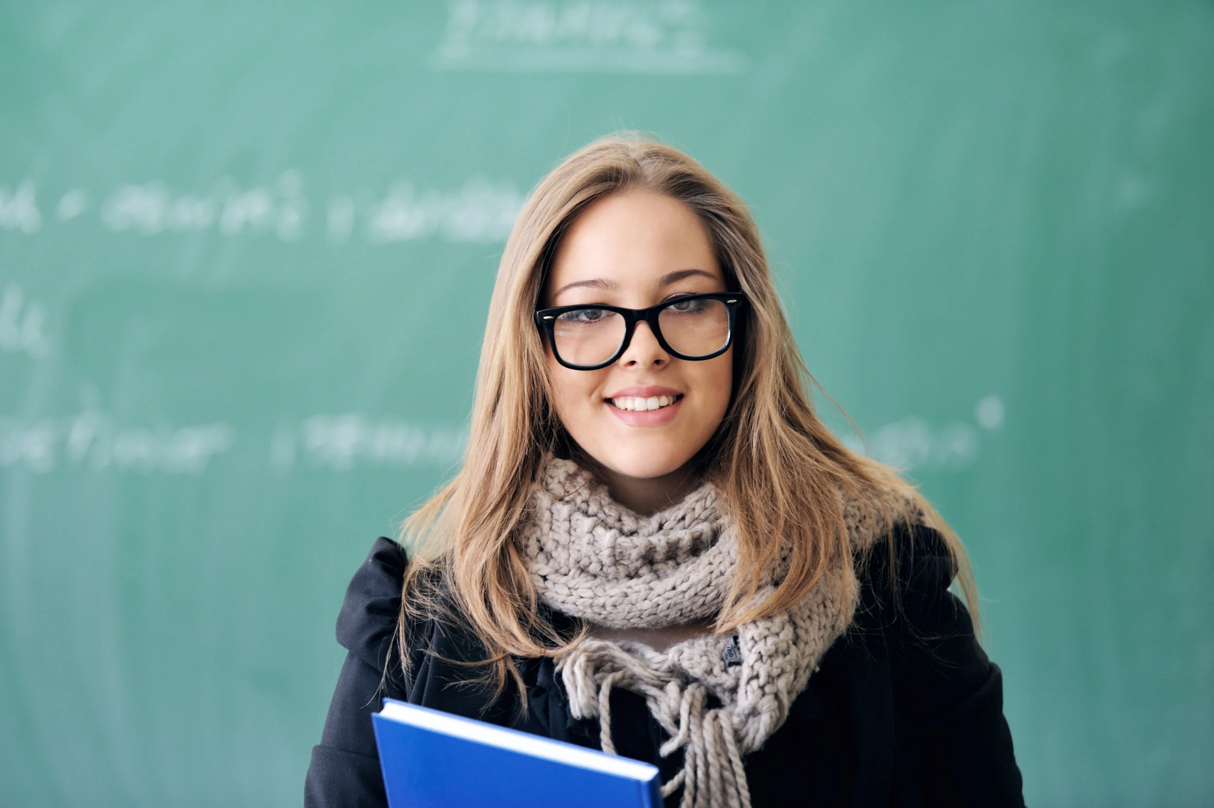 smiling-schoolgirl-holding-a-book-in-front-of-blackboard_HF35HJ0Bo.jpg