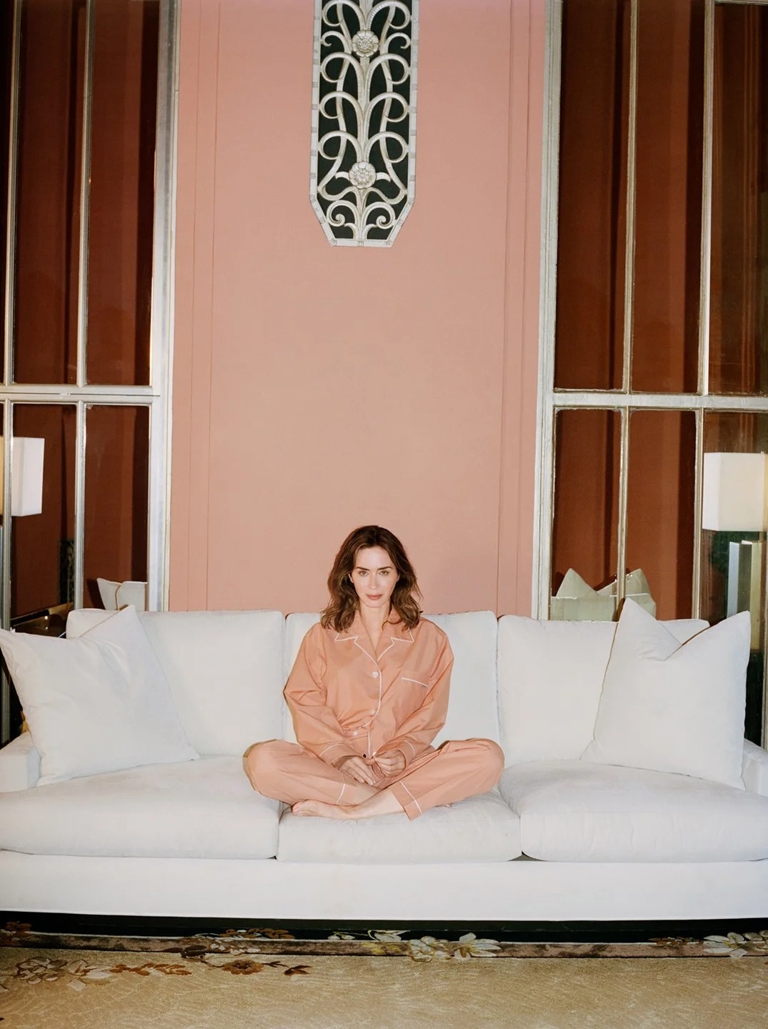  Emily Blunt seated on a bed in a pale dress at the Waldorf Astoria in New York City for WSJ Magazine, photographed by Sean Thomas. 
