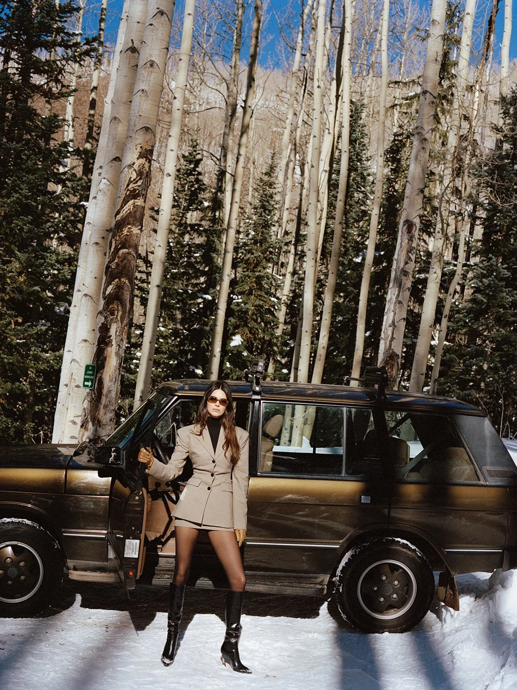  Kendall Jenner in a neutral après-ski look beside a black SUV in an Aspen forest for FWRD, photographed by Sean Thomas. 