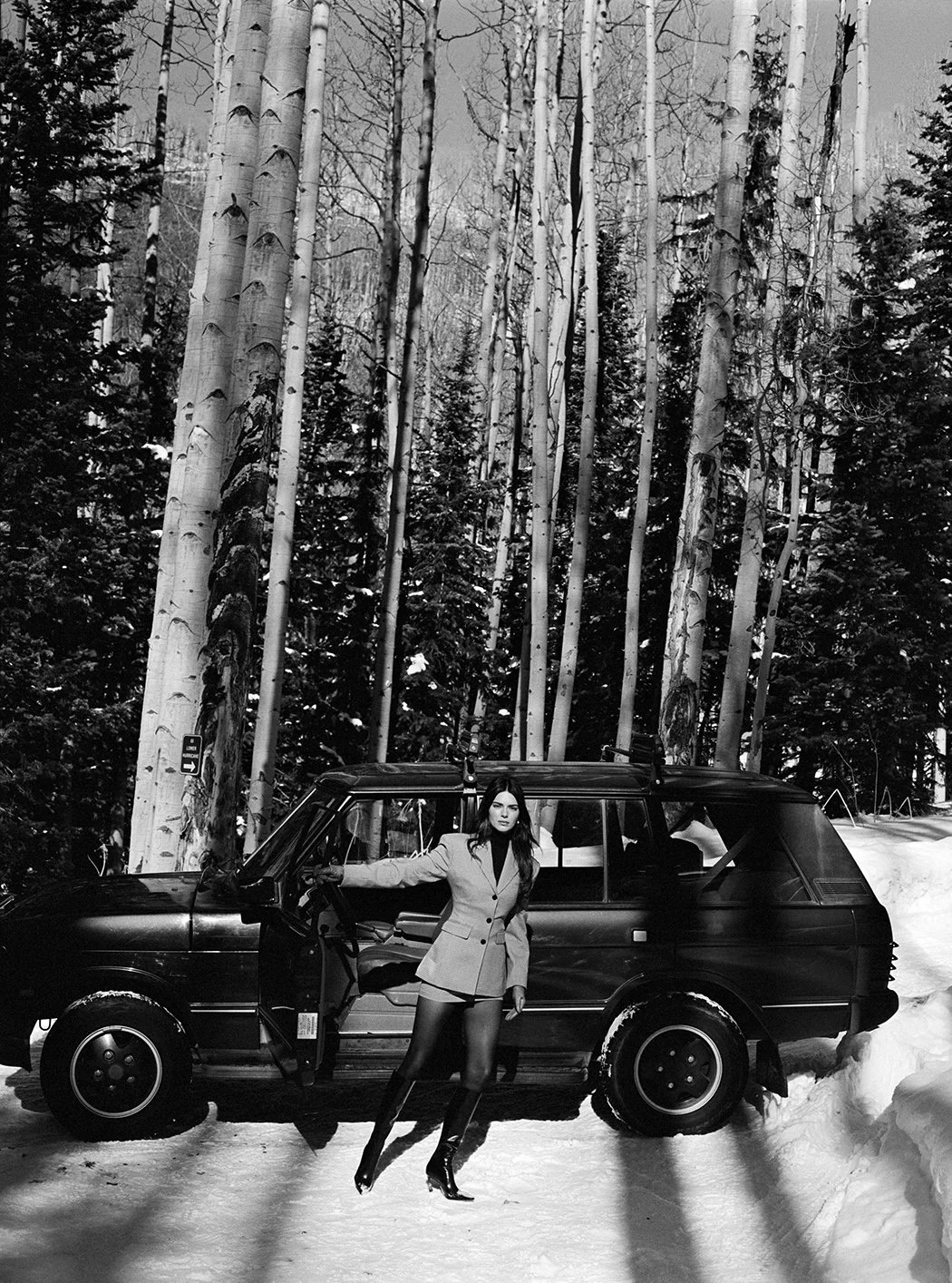  Black-and-white portrait of Kendall Jenner in a tailored jacket beside a black SUV in an Aspen forest for FWRD, photographed by Sean Thomas. 