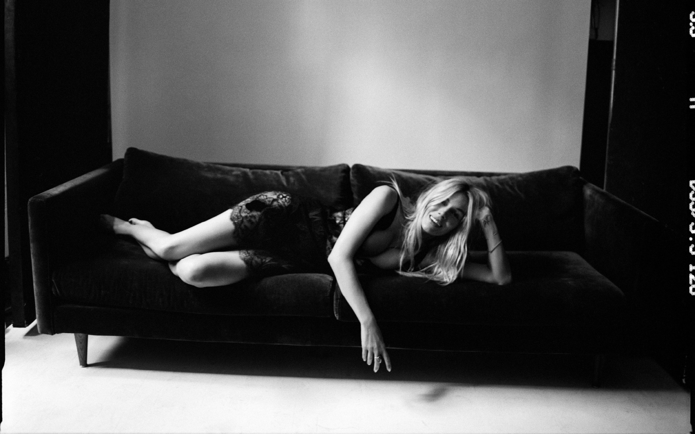  Black-and-white portrait of Sienna Miller reclining barefoot on a dark sofa in black lace, photographed by Sean Thomas for HTSI. 