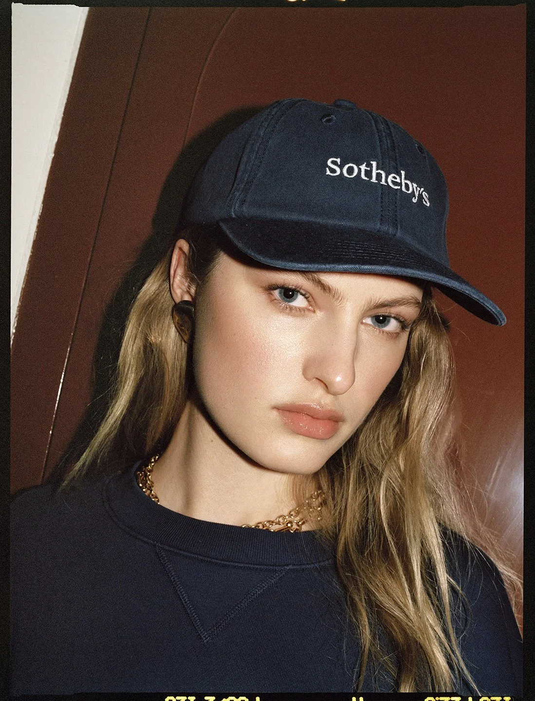  Close portrait of Felice Nova Noordhoff wearing a navy Sotheby’s cap and sweatshirt, photographed by Sean Thomas for FRAME. 