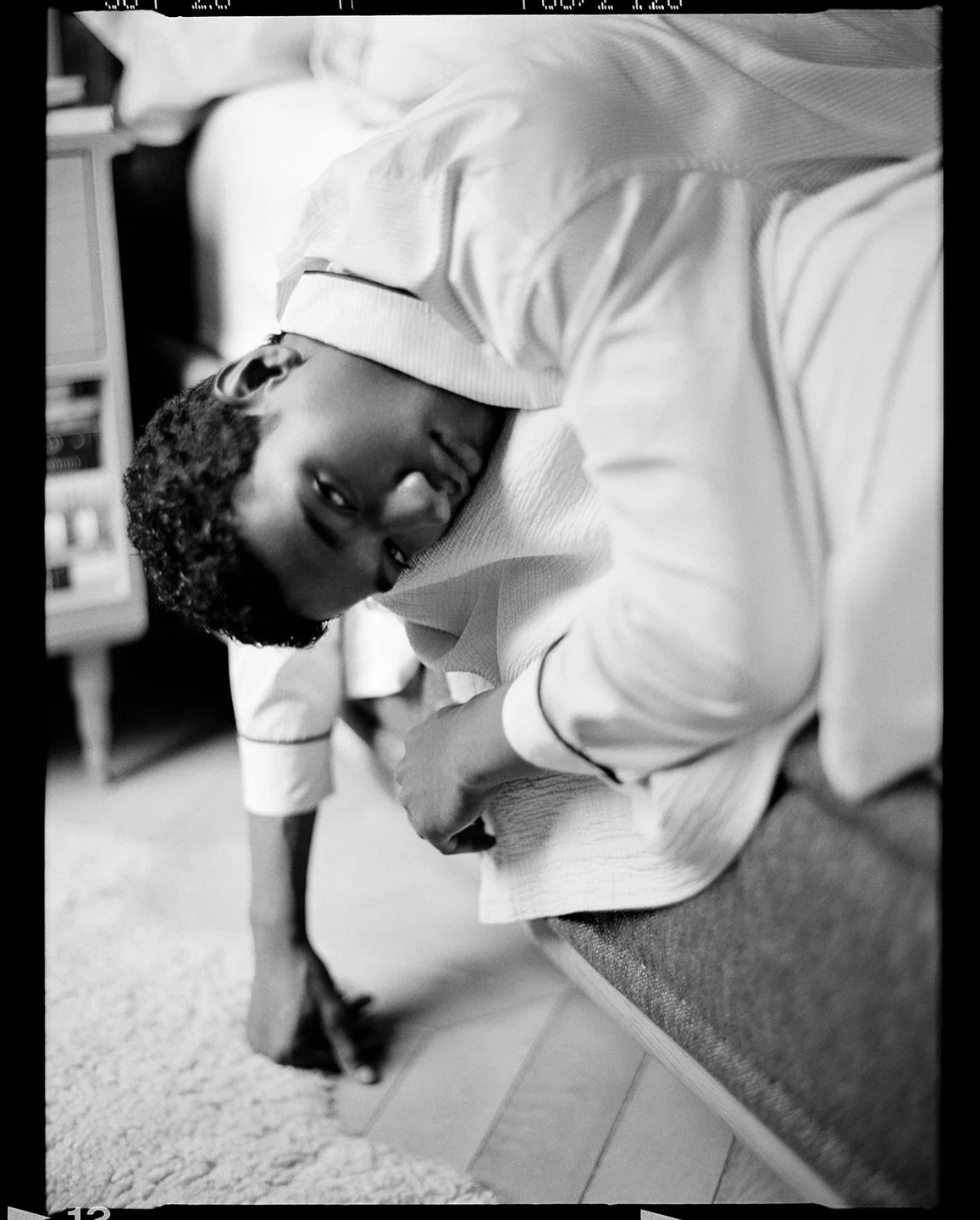  Black-and-white portrait of Joshua Seth Williams reclining indoors in white knitwear and trousers, photographed by Sean Thomas. 